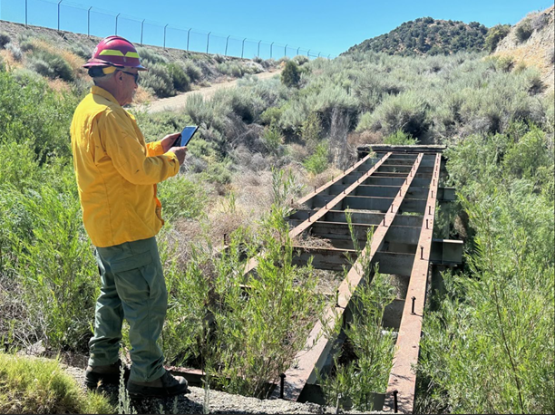 Image showing Burned Area Emergency Response Specialist Casey Shannon evaluating a culvert under the remains of old road bridge in the Post Fire burned area on the Los Padres National Forest