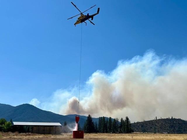 Helicopter dipping bucket from portable water tank with smoke in background from Shelly Fire