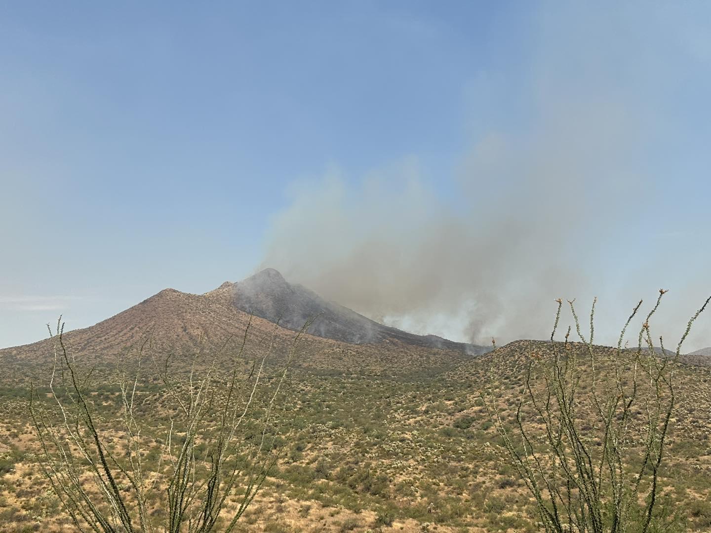 Smoke rising from a peak against a blue sky with desert vegetation