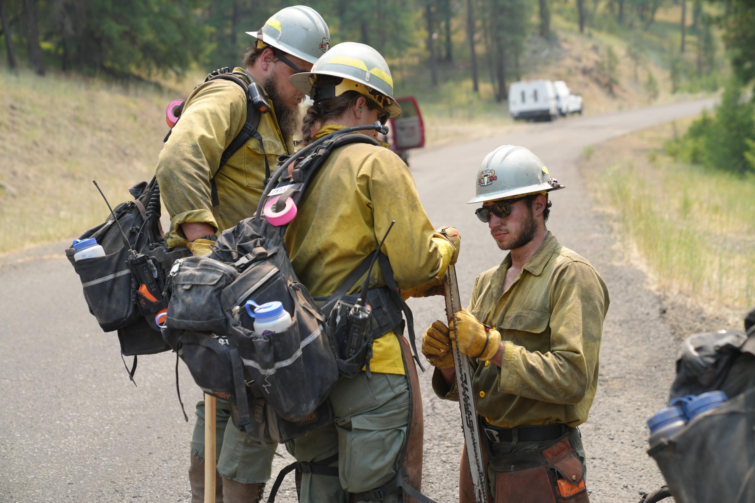 Three firefighters standing on a road fixing a chainsaw chain