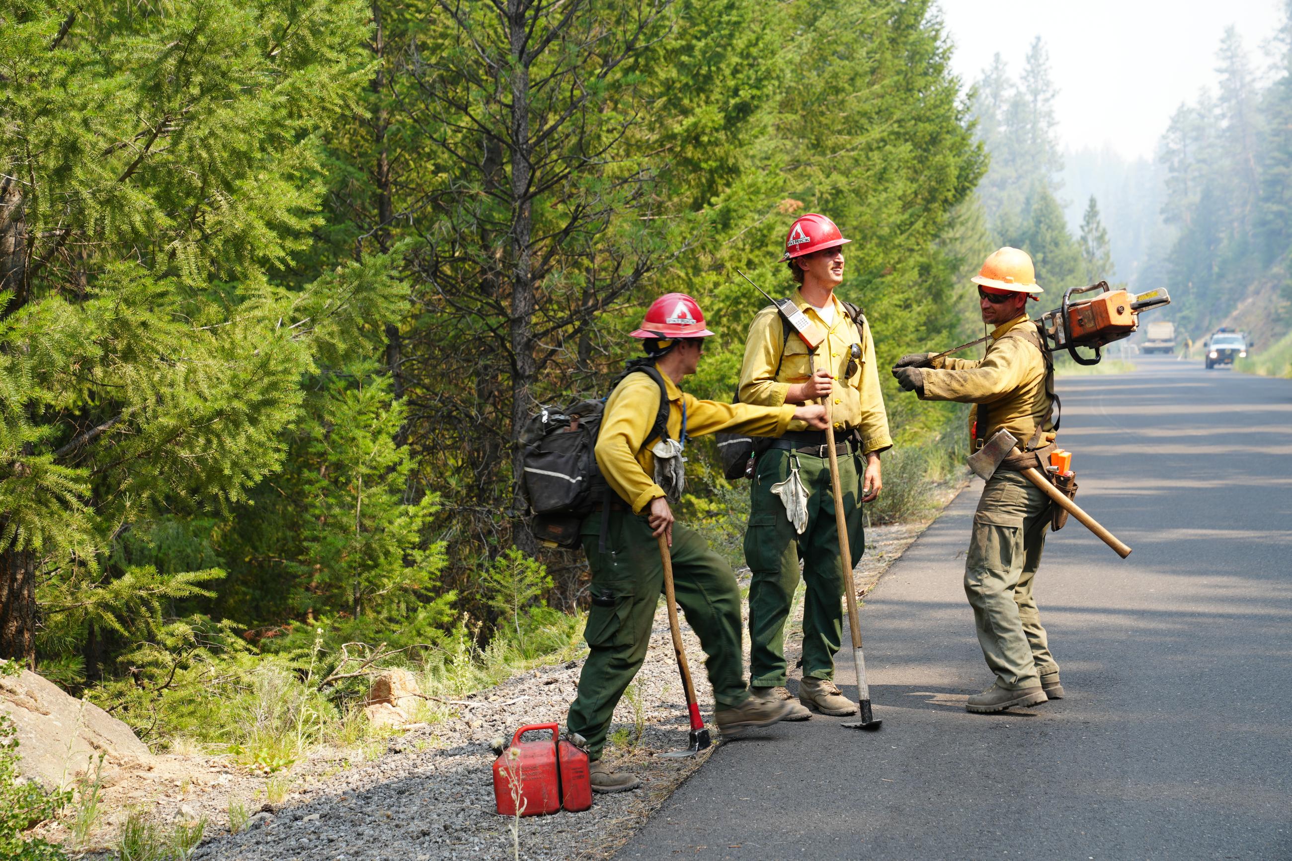 Three firefighters standing on a road holding chainsaws