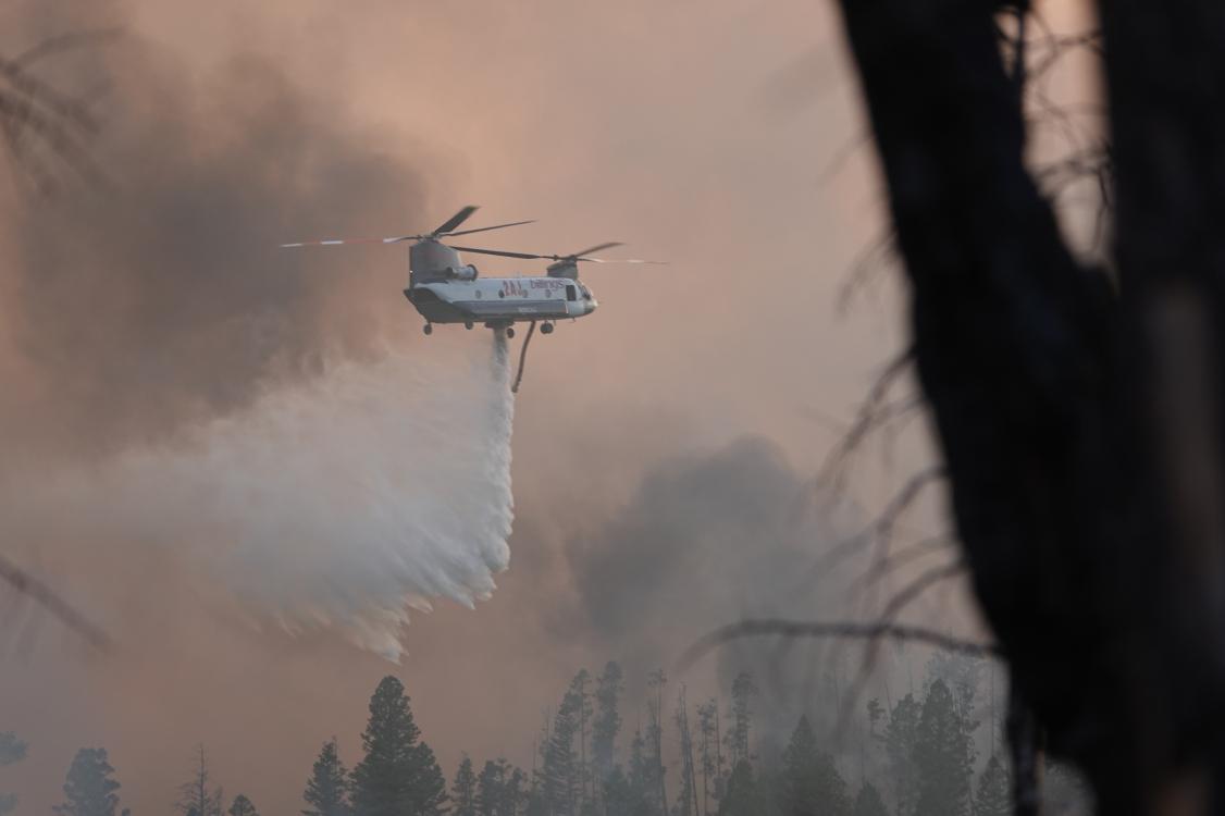 Large helicopter dropping stream of water with dark smoke in background