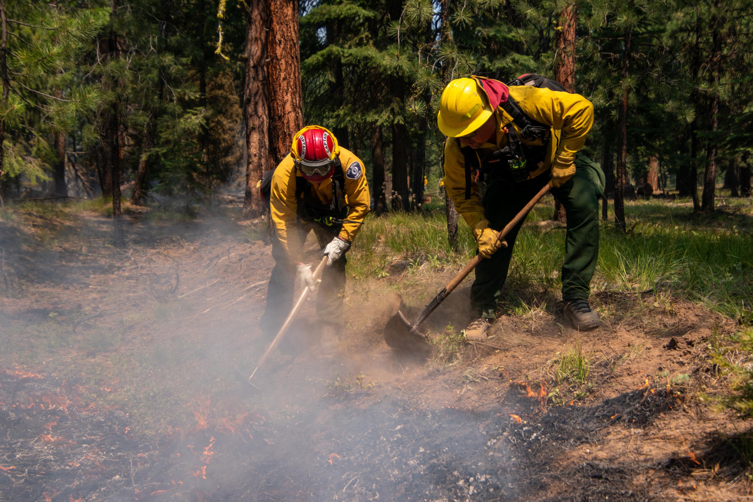 Two firefighters with tools spreading hot ashes and fire 