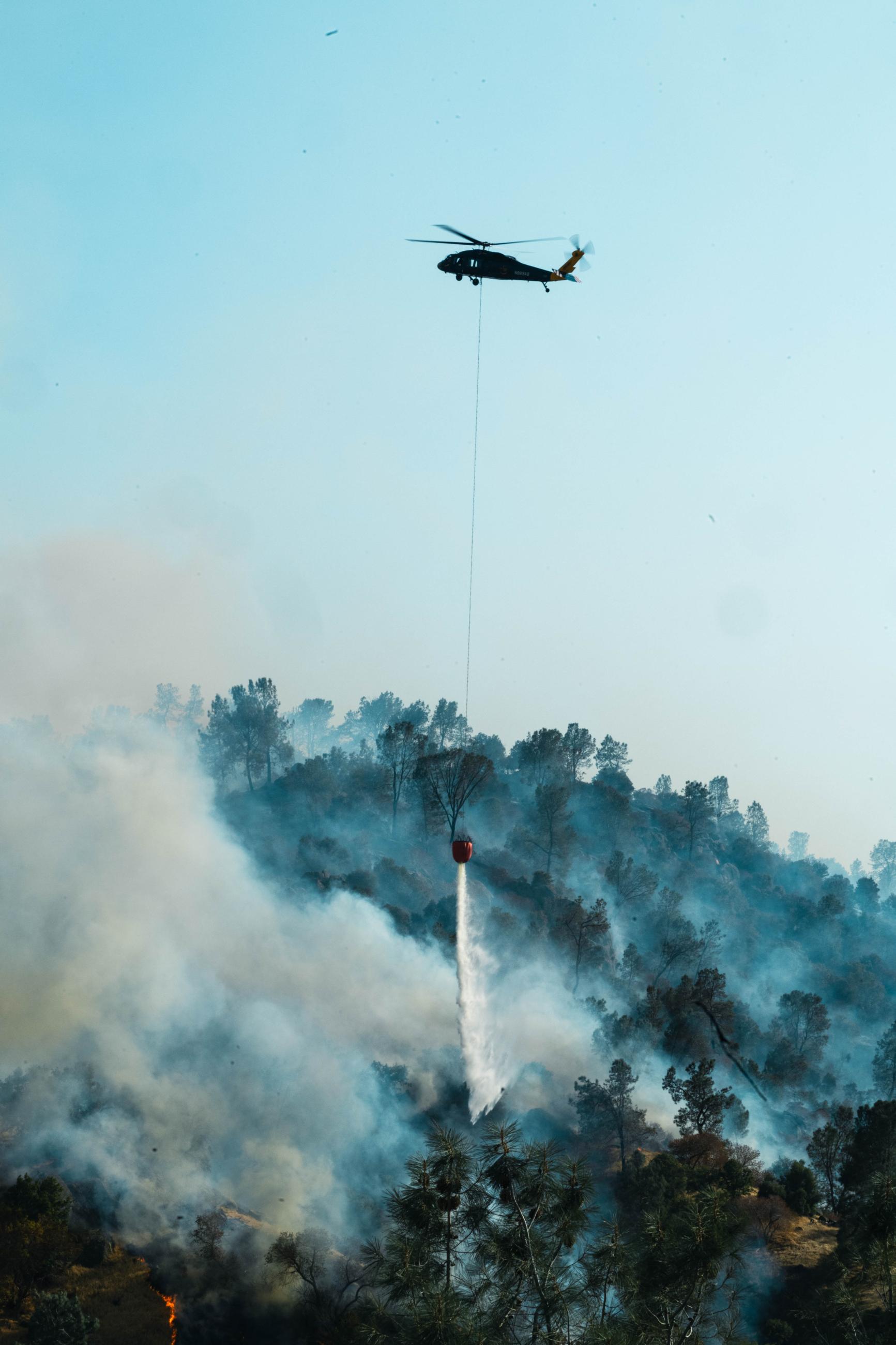 helicopter dropping water on a fire with snoke