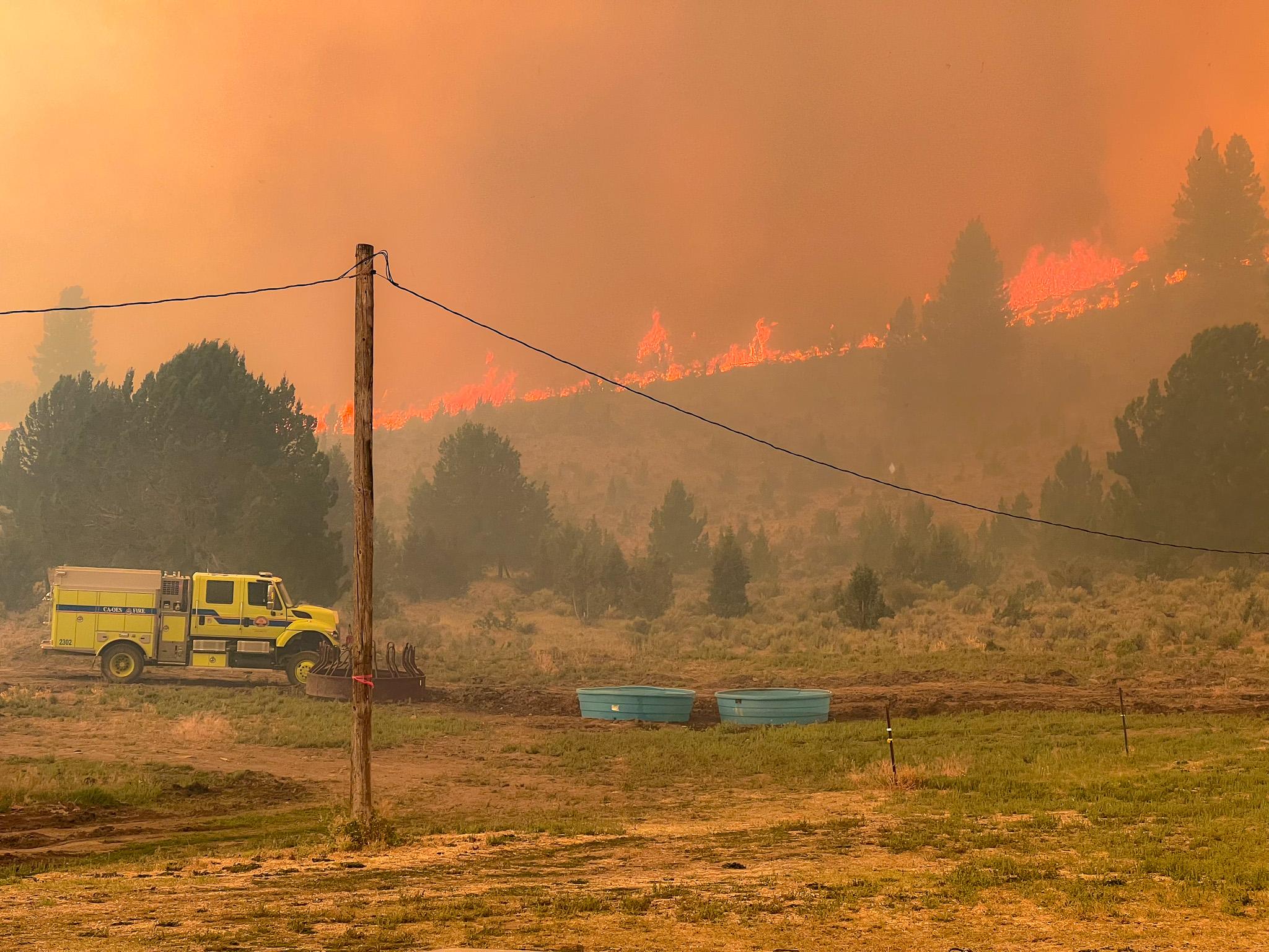 Engine in front of ranch. Hills burning in background. 