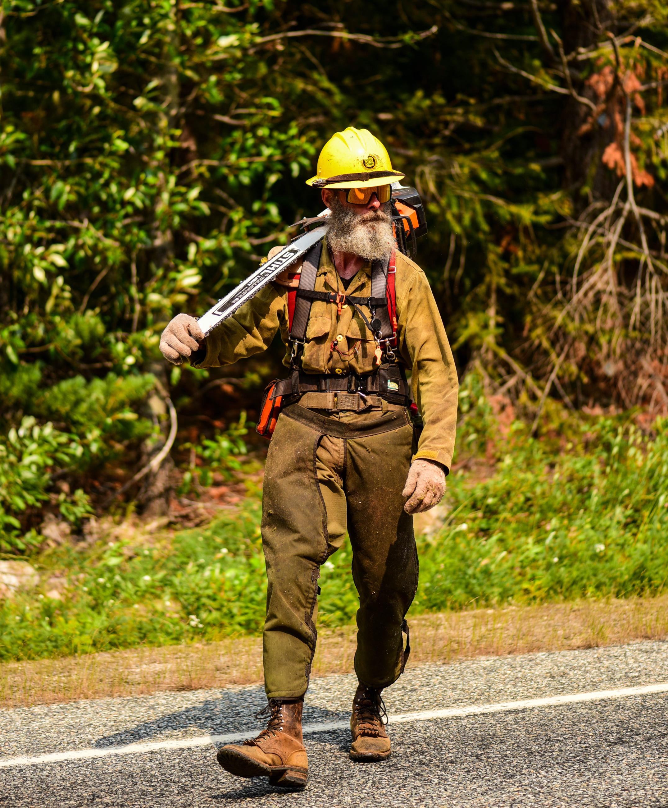 Man in fire gear walking with a chainsaw over his shoulder