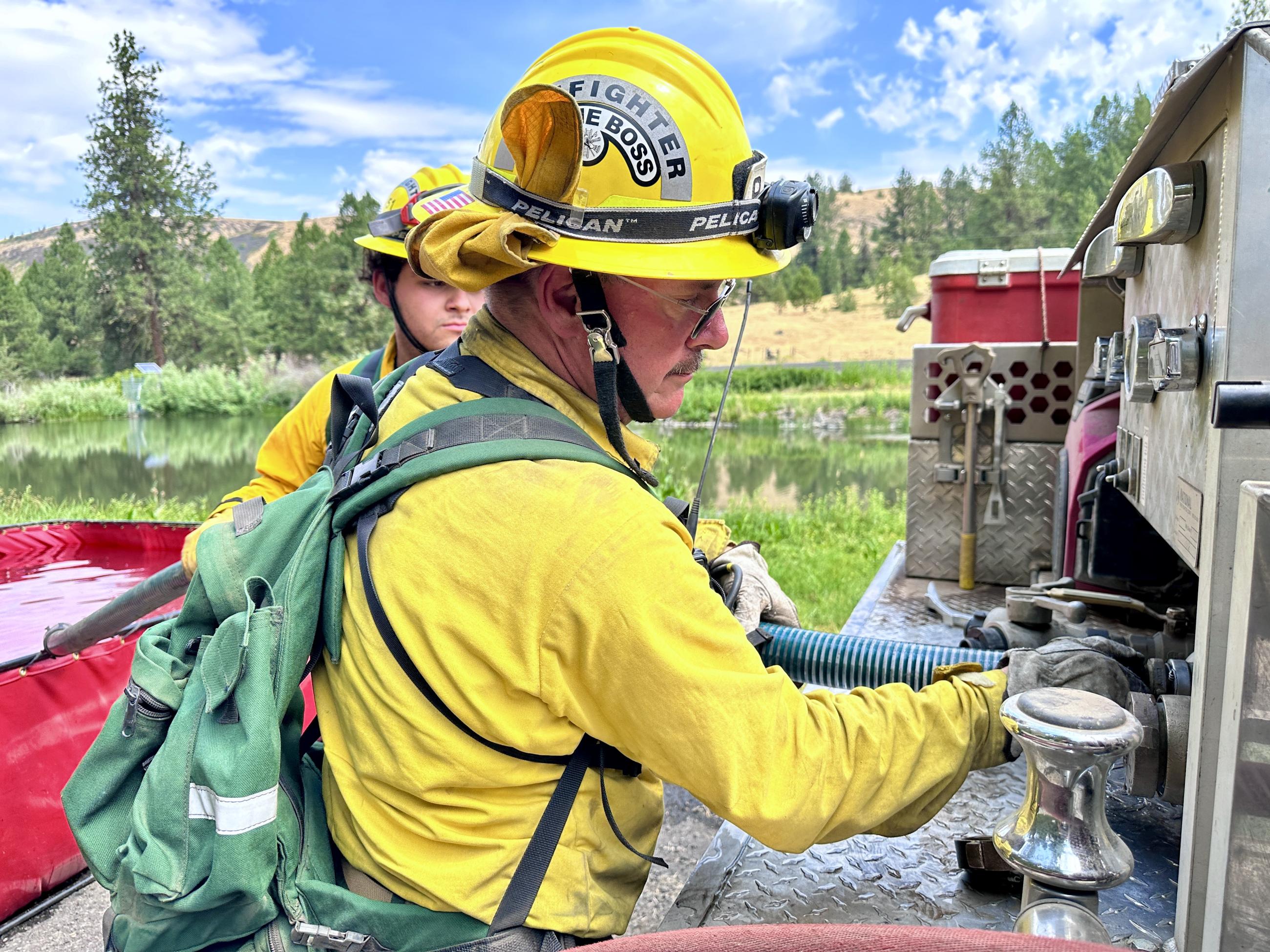 An engine boss wearing yellow nomex connects a hose to the engine