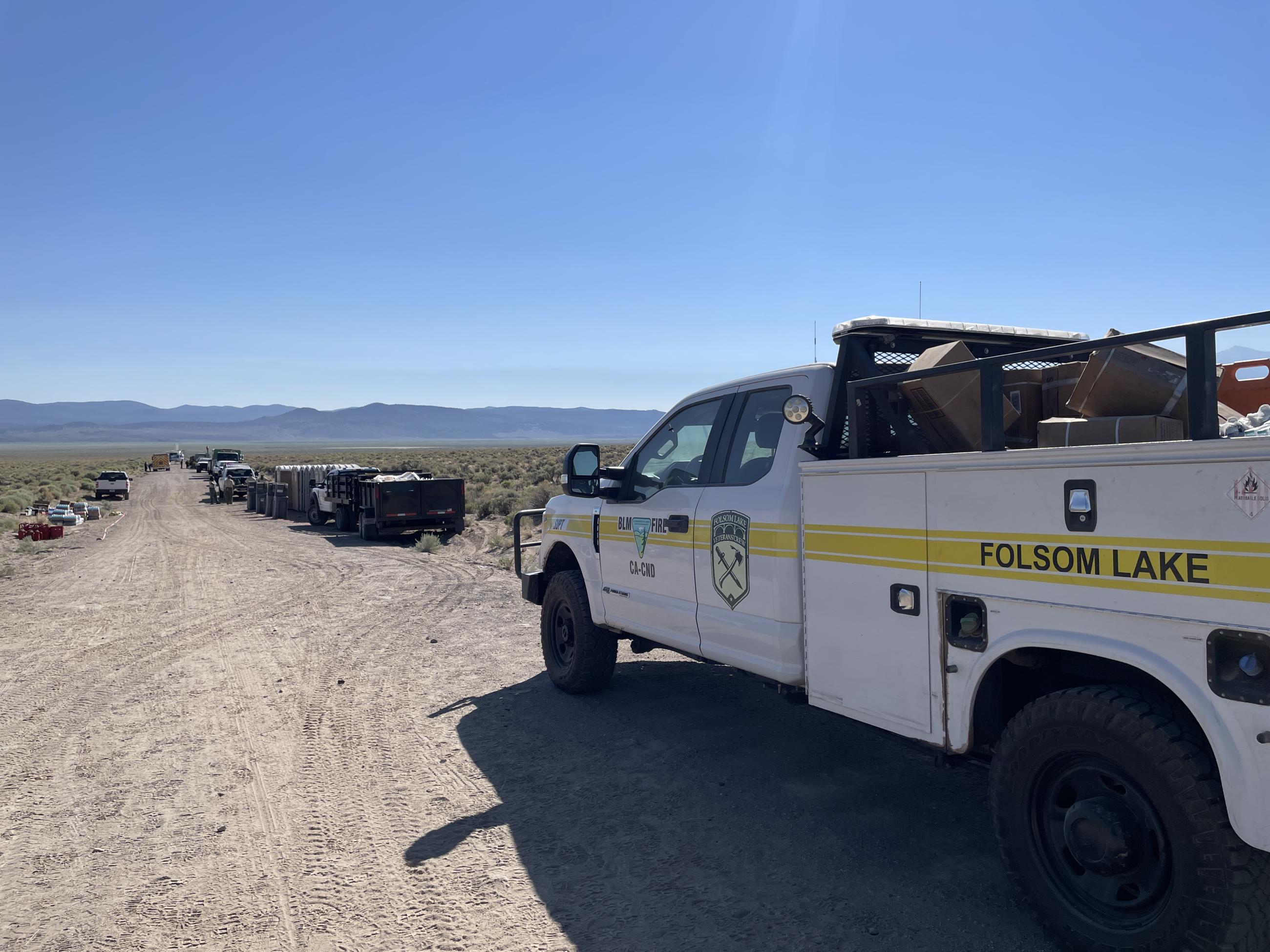 White work truck with yellow strip and Bureau of Land Management fire emblem parked on side of dirt road.