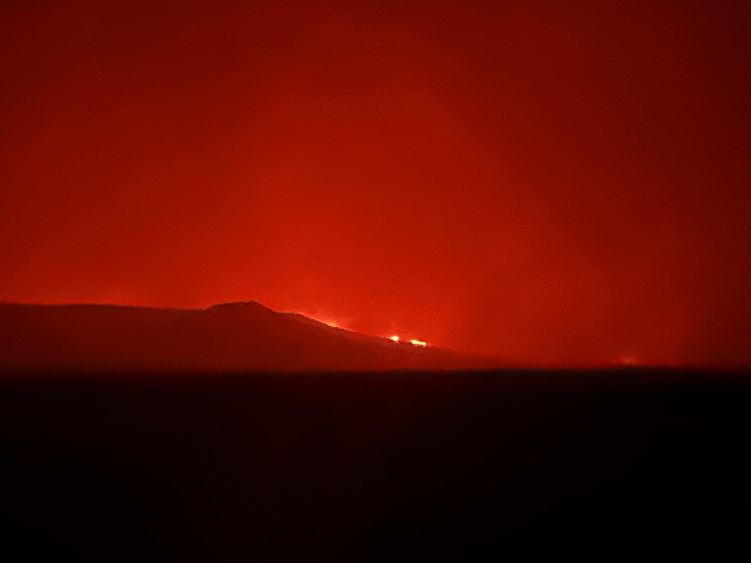 Red Glow of fire in night sky flames just visible over hill