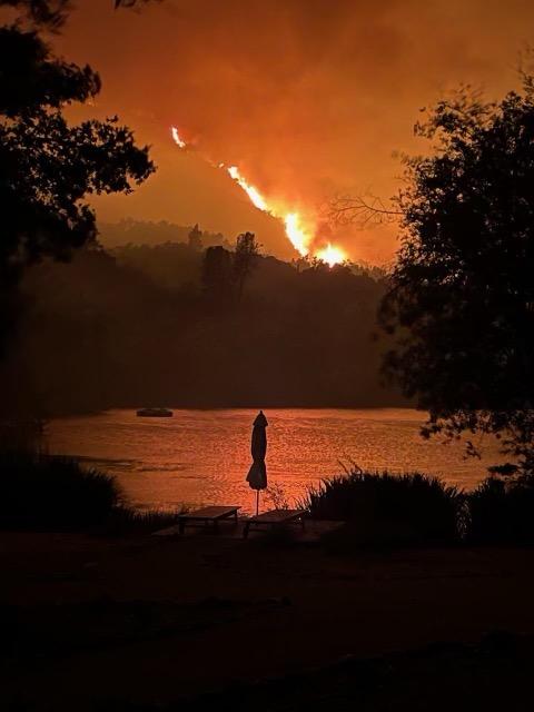 Flames burn along a ridgeline above a reflective lake.