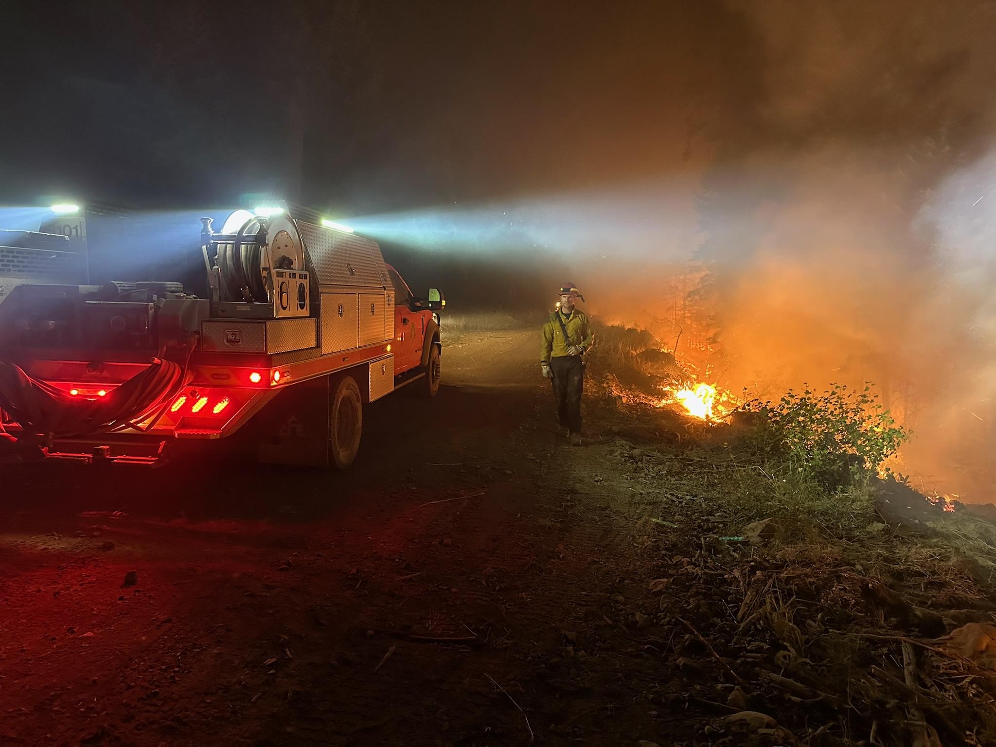 A firefighters sprays water out of hose at fire burning at night