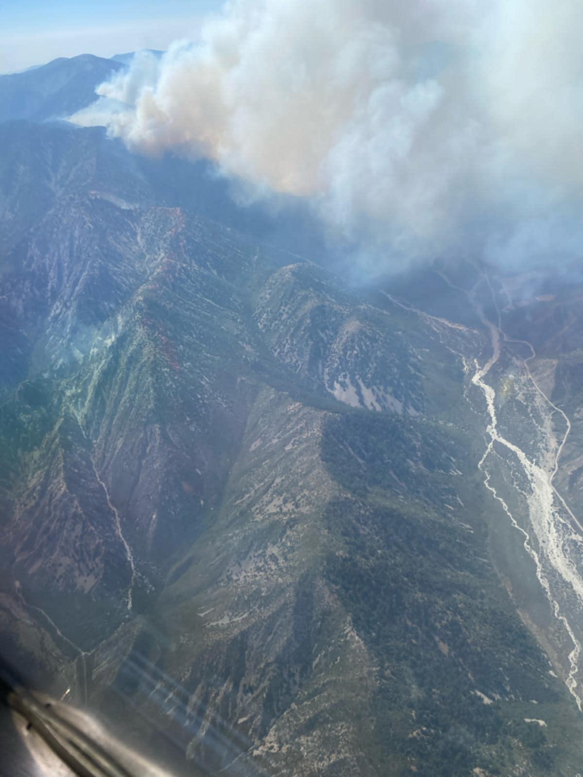 White smoke rising from active fire behavior in a mountainous landscape.