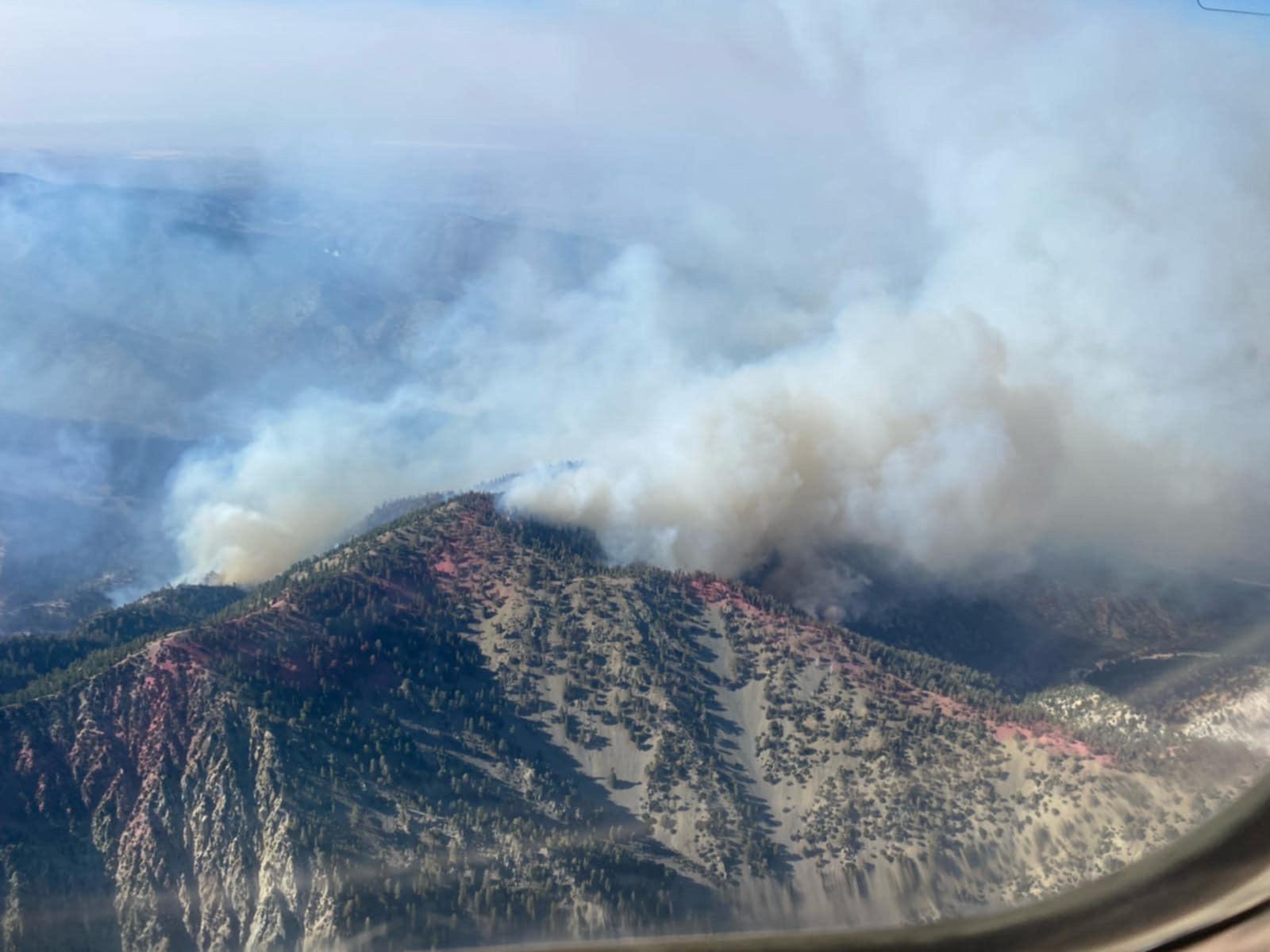 White smoke rising from active fire behavior in a mountainous landscape.