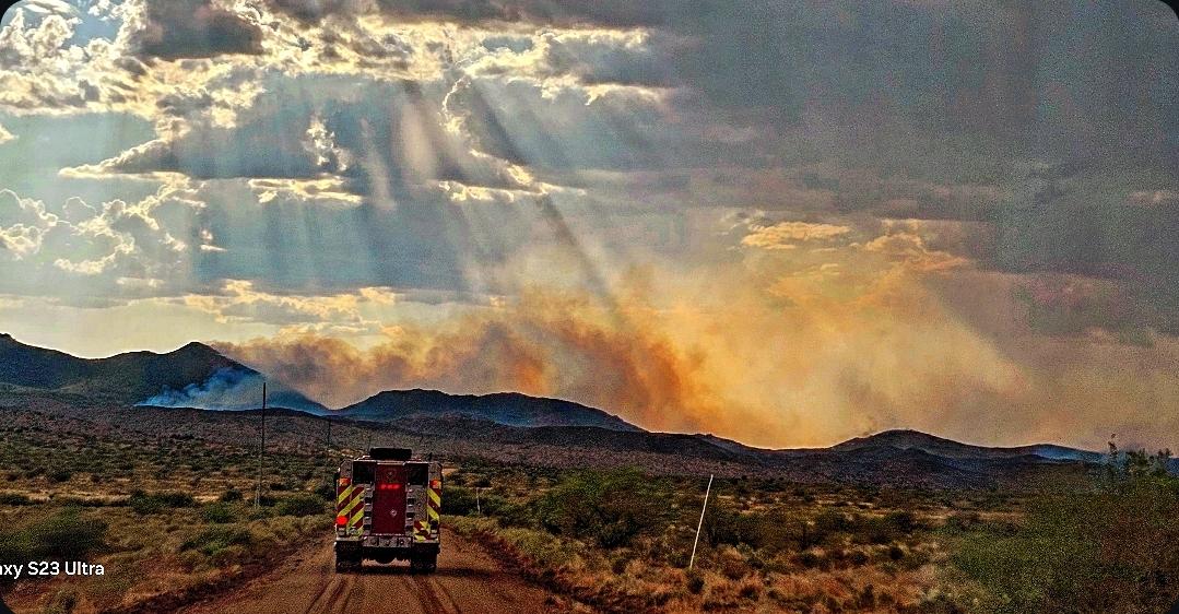 Engine driving dirt road with smoke rising in distance 