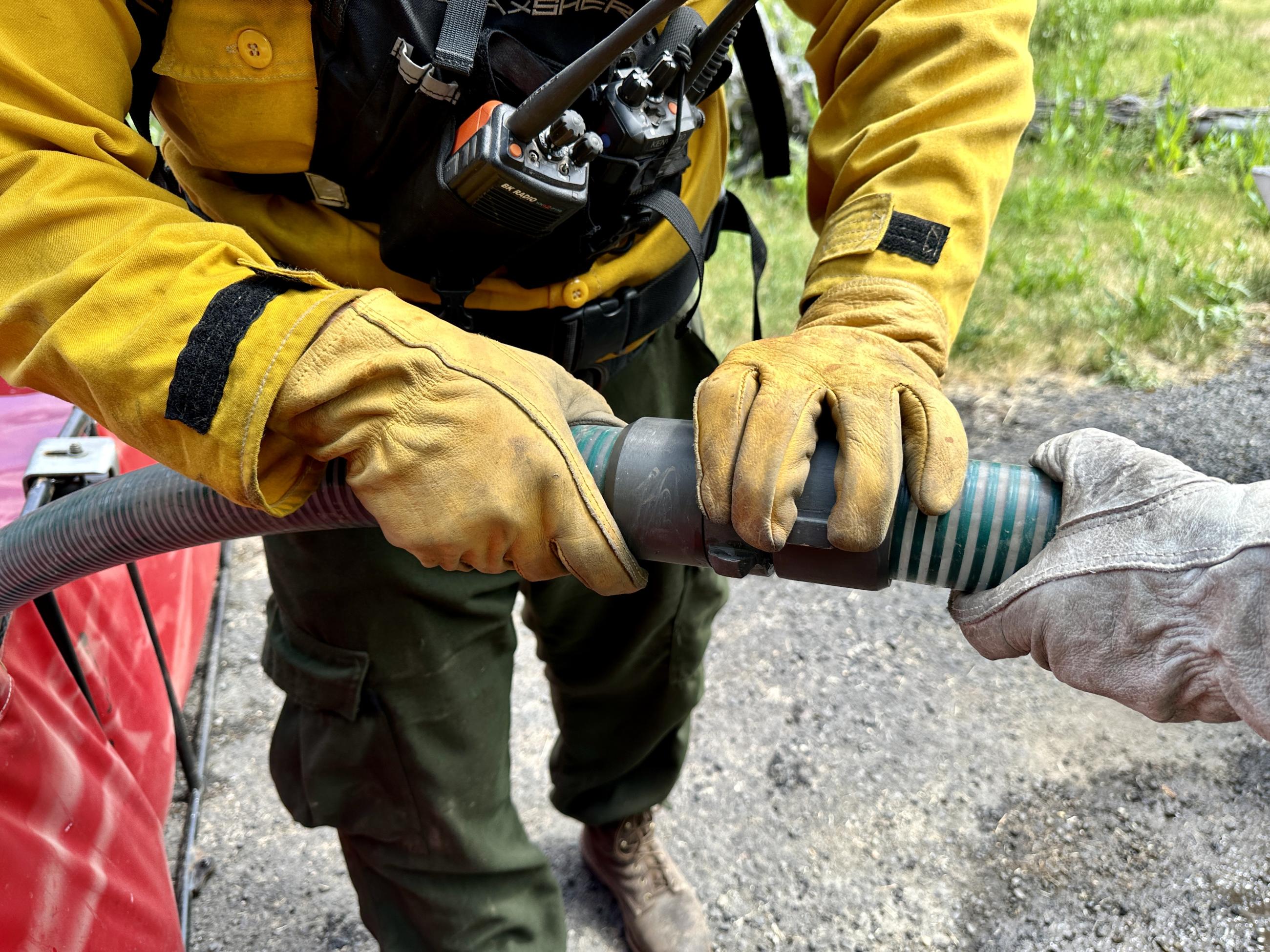 A firefighter wearing yellow nomex holds a hose with the help from another firefighter.