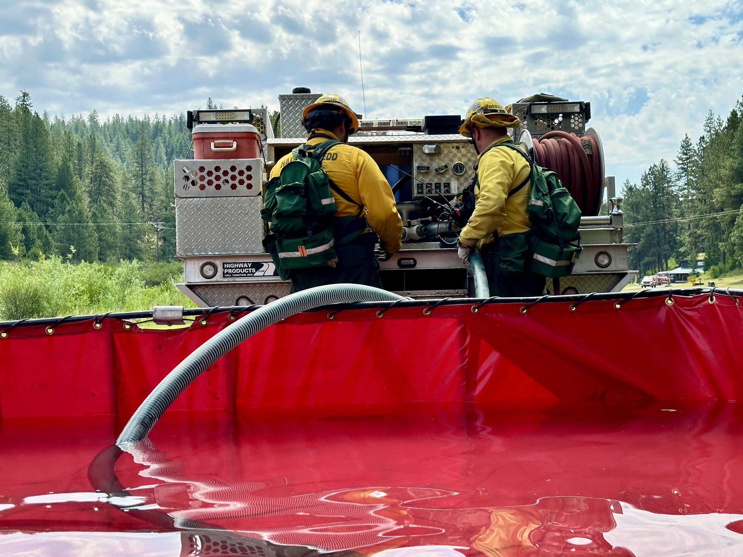 Fire personnel draft water from a portable water tank to fill up a type 6 wildland fire engine in behind them.