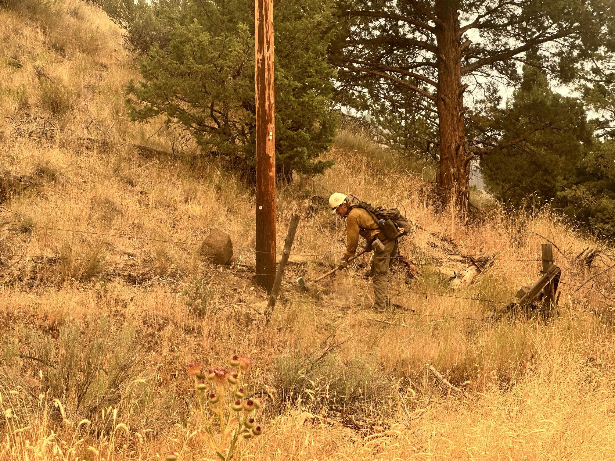 A firefighter digs a line around a utility pole