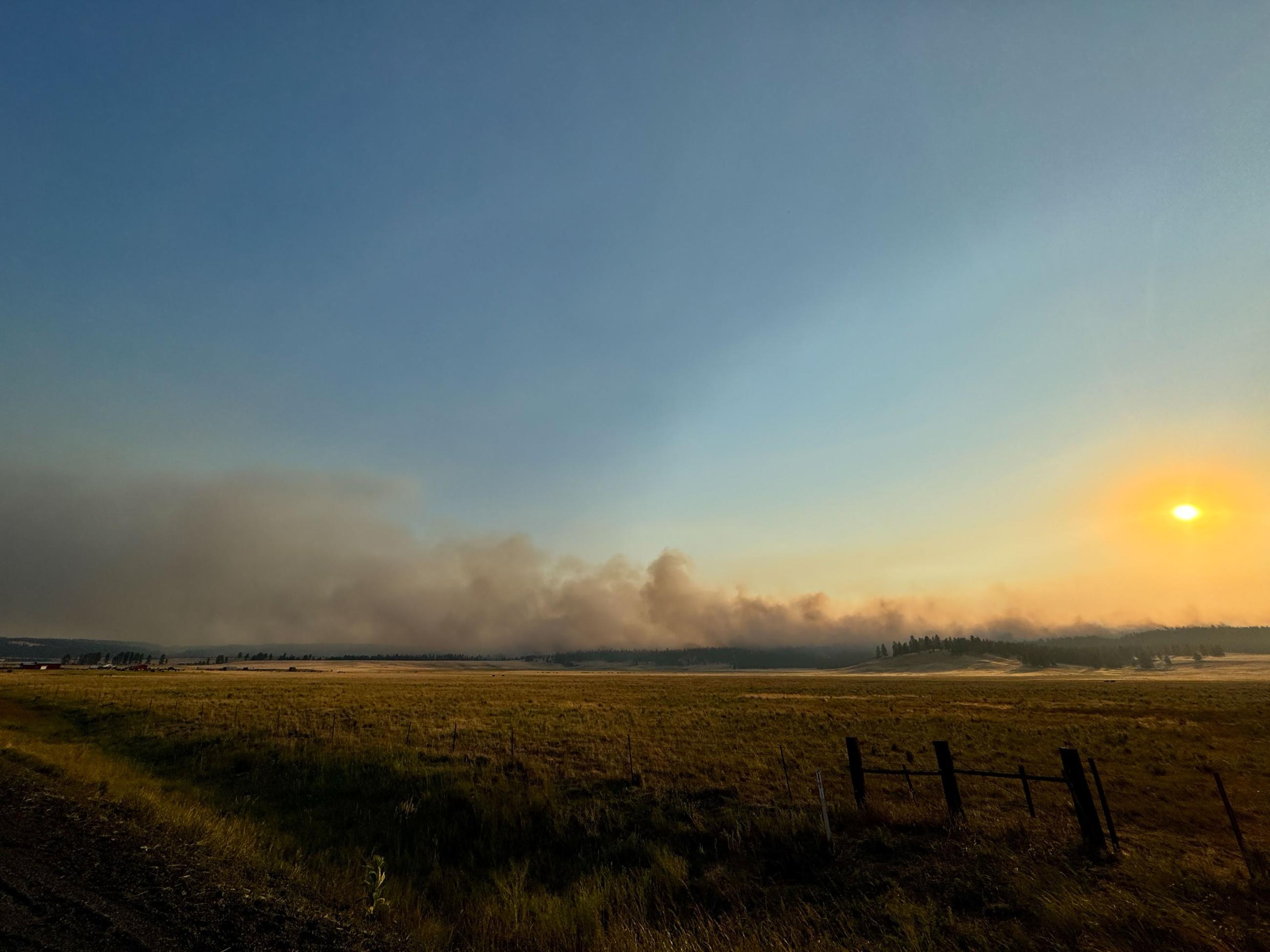Smoke rising with a sunset and grasslands in the foregrand. 
