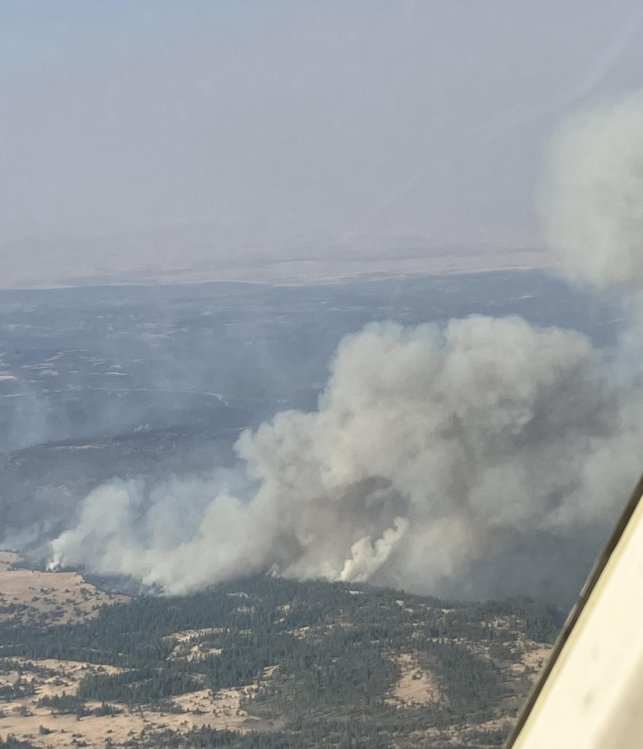 The aerial view of the Lone Rock Fire shows a column burning and the wing of an airplane in the foreground.