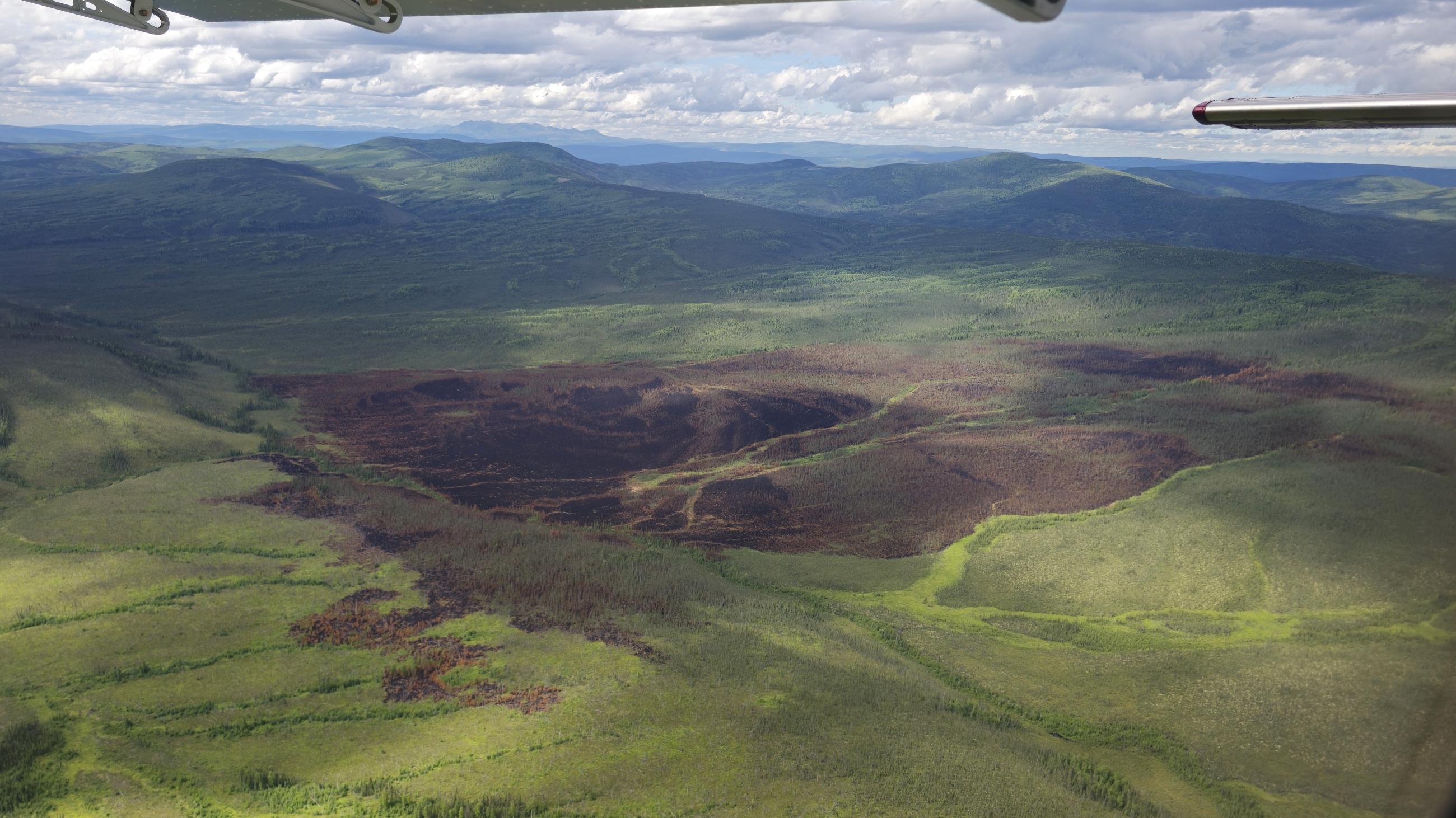 round black and red burn in green and moutains from a plane