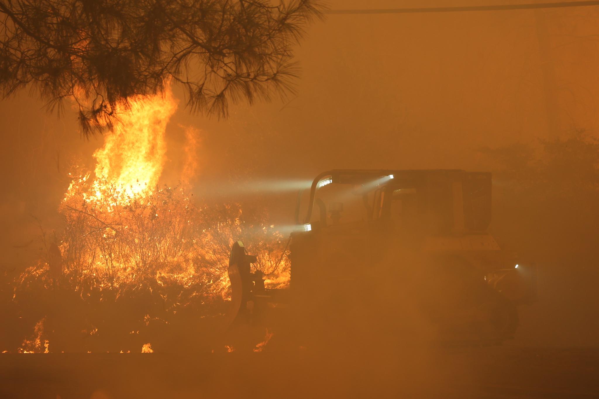 A bulldozer can barely be seen through thick orange smoke and flames.
