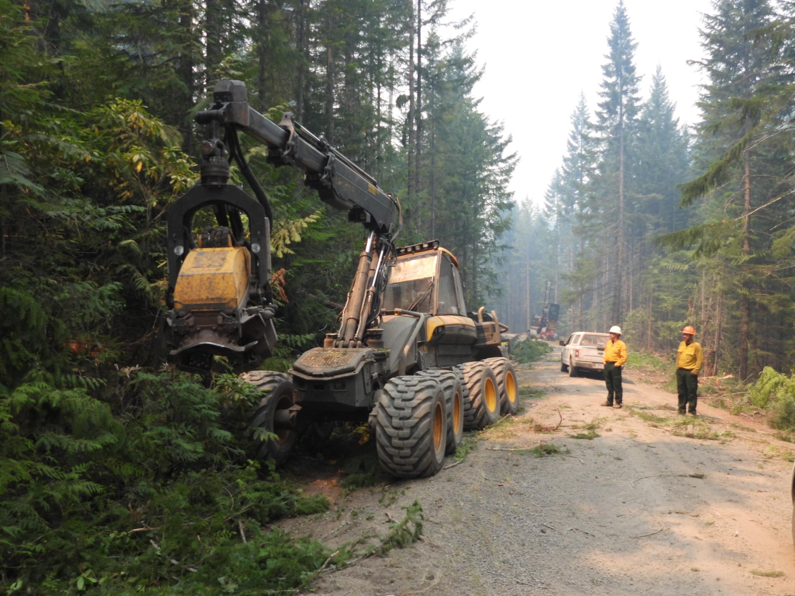 a piece of logging equipment removes brush along the side of a road to widen fireline, July 30