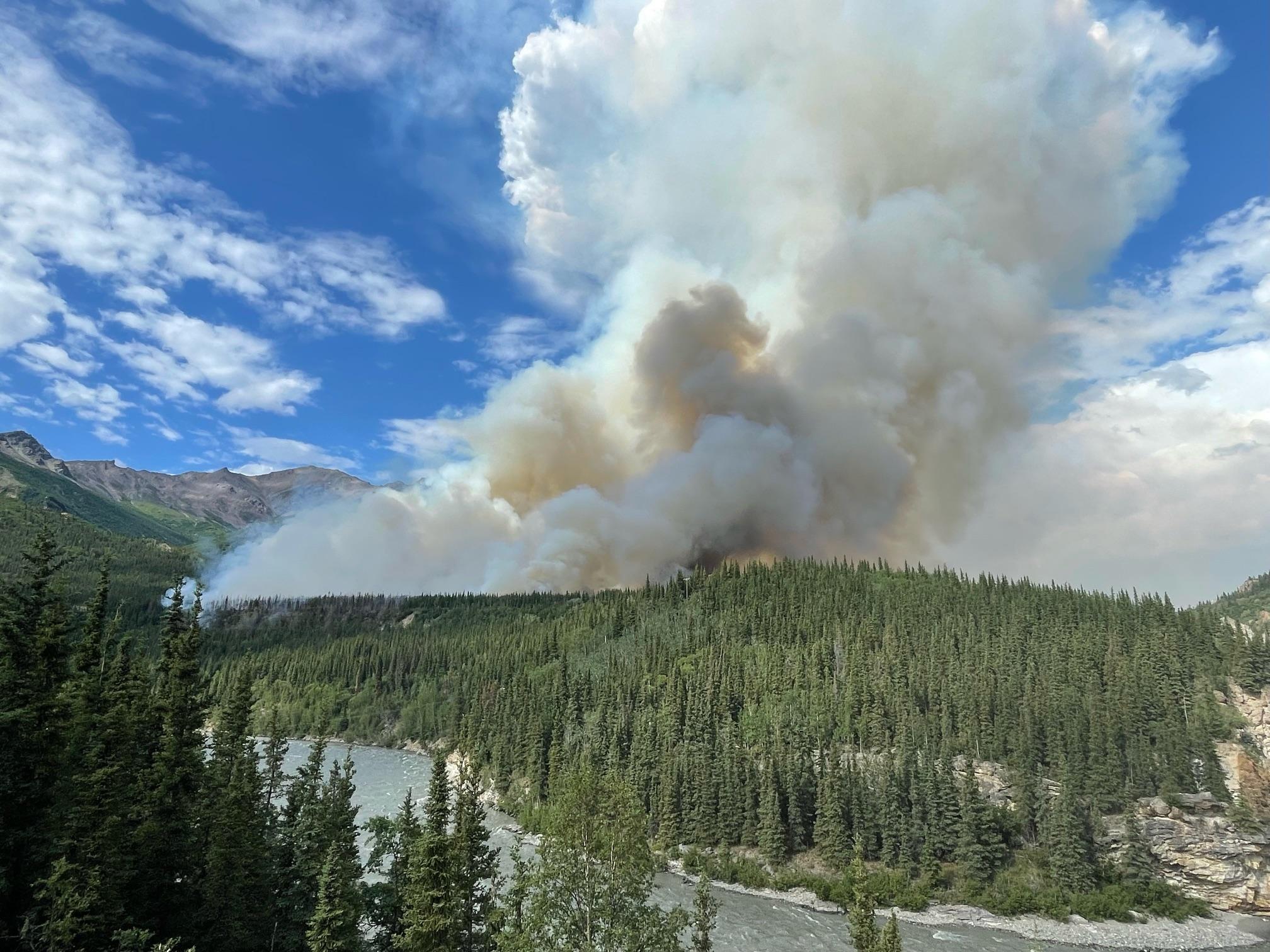 A large smoke plume rises from a river canyon.