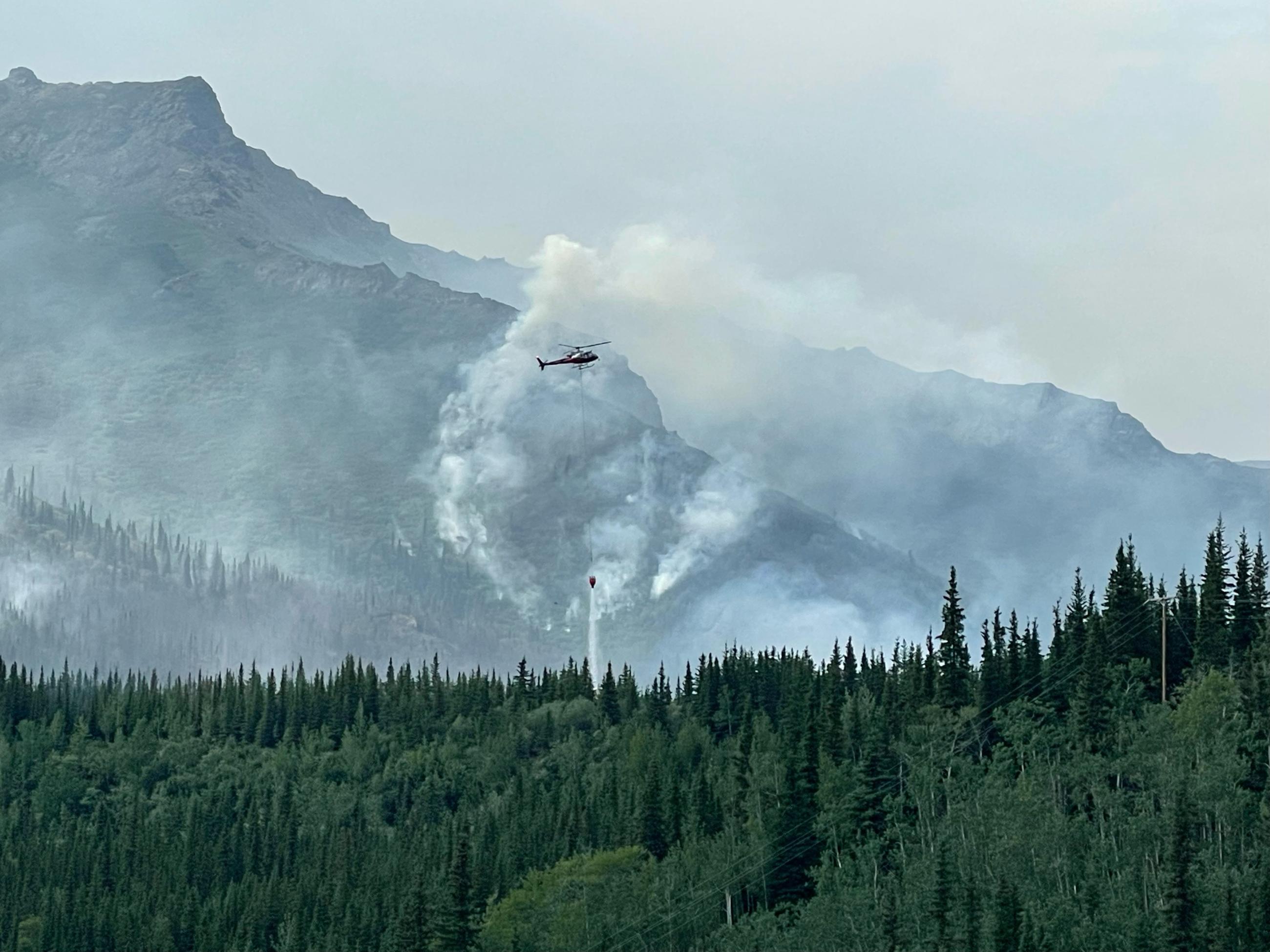 A helicopter flies through smoke to drop water on the fire.