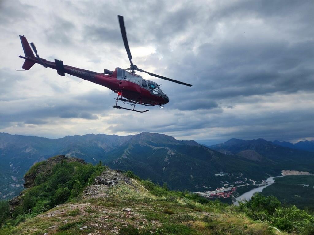 A helicopter rises above a clearing that serves as a heliport.