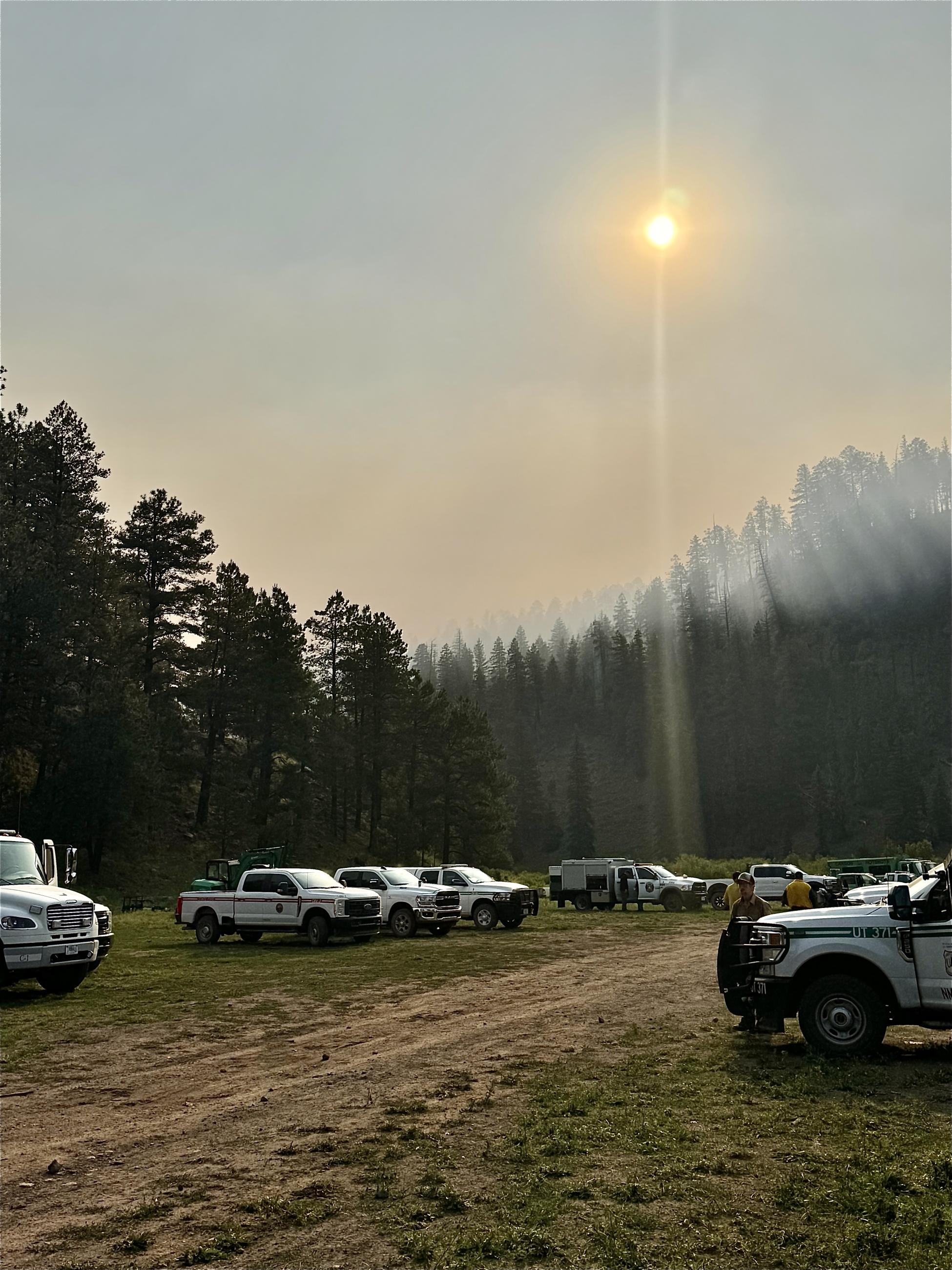 Fire vehicles along dirt road with Ridge Fire in the background and smoke blocking out the sun.