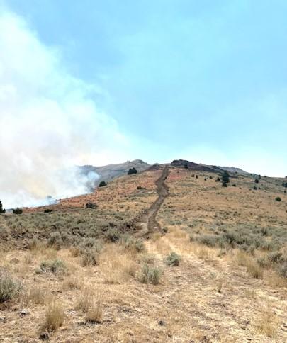 Dozer line along a ridgeline in a grassland, with wildfire smoke rising to the left of the line