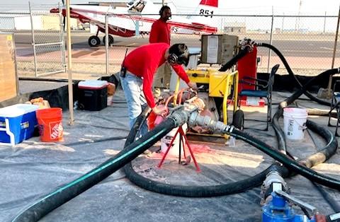 Technician adjusting equipment as retardant is prepared to be loaded into aircraft via a tube. Aircraft also shown in photo, in background.