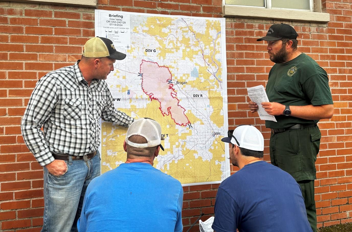 Four people talking while viewing a map adhered to a brick wall