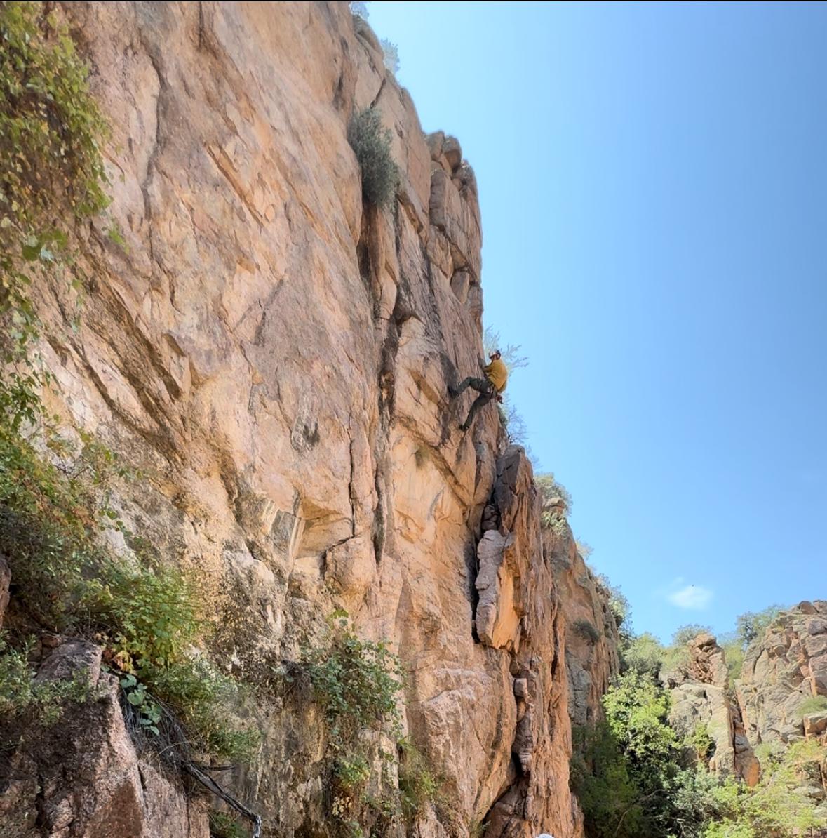 A person in firefighter yellows repels down a red rock face.