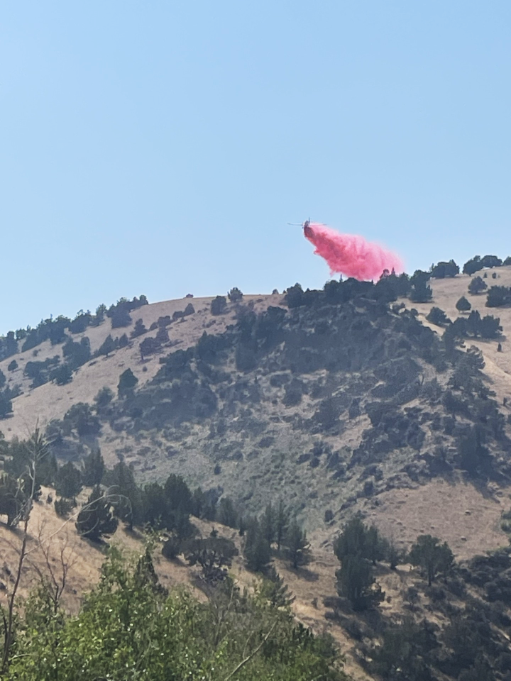 Airplane releasing retardant (red) as it crests over a shrubland hilltop