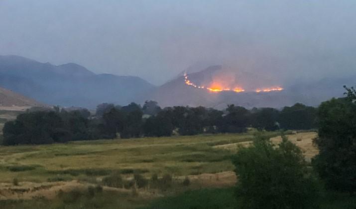 Flames along the midsection of a mountain, with a rangeland in front of it. Hazy morning lighting
