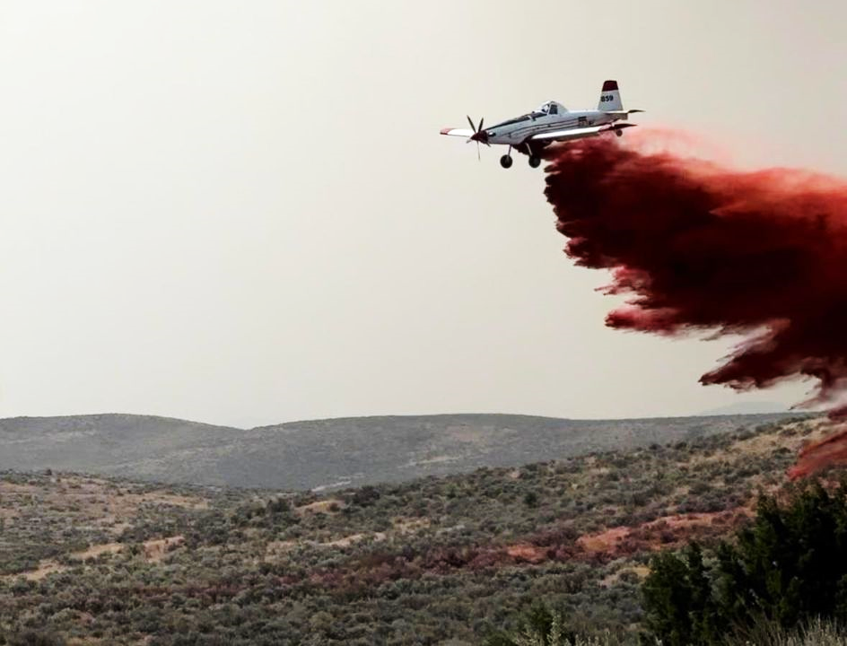Airplane releasing retardant (red) with active fire shown