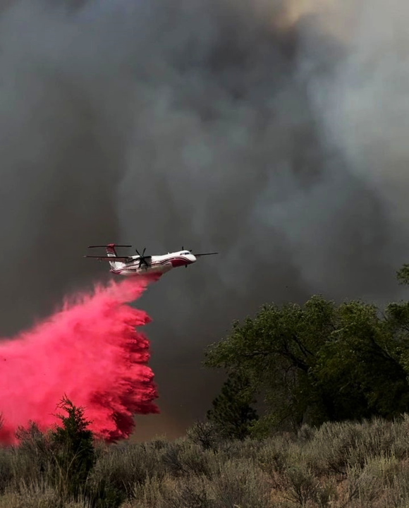 Airplane releasing retardant (red) with black clouds behind it