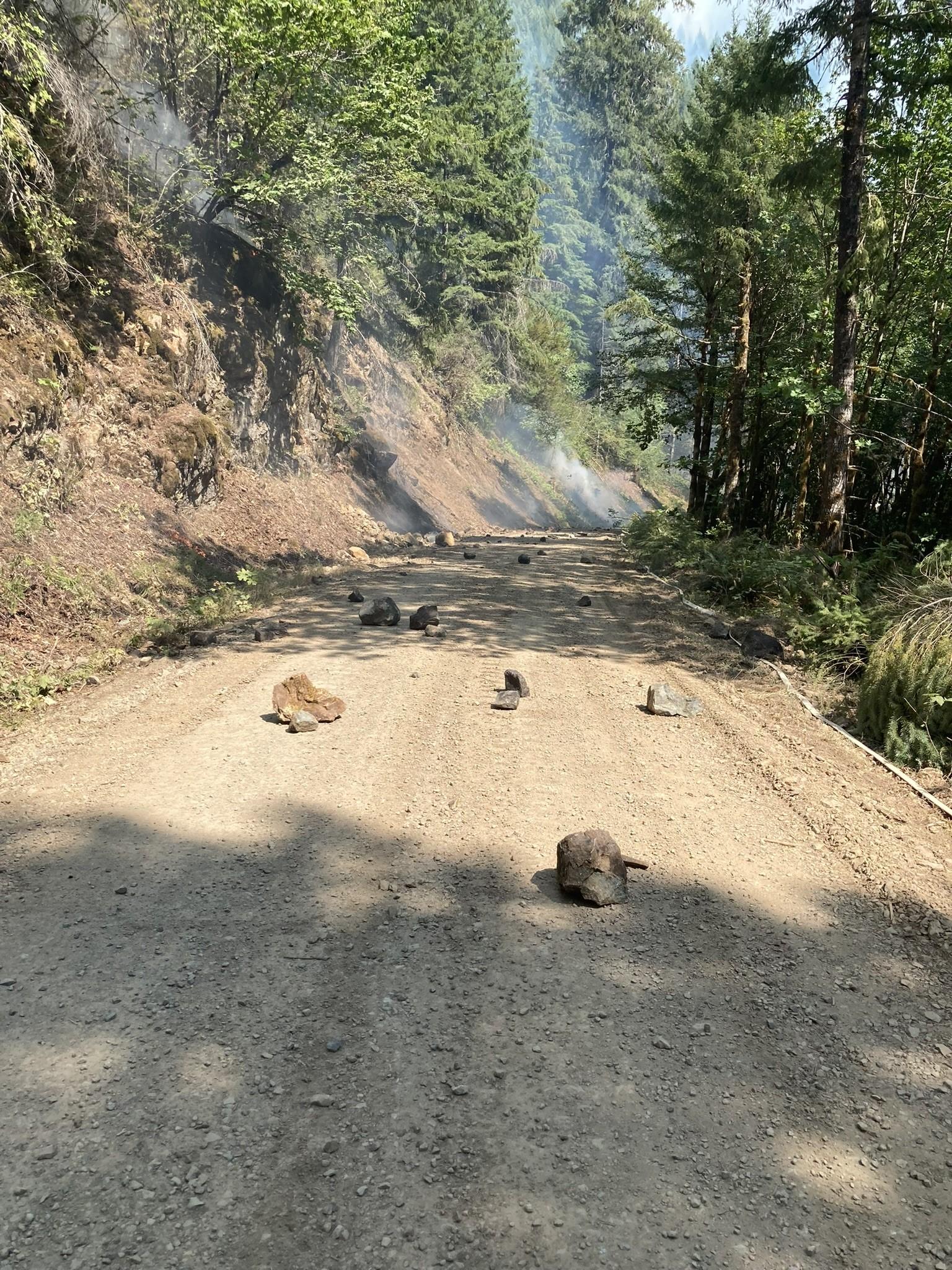 A dirt road is seen with rocks of varying sizes scattered in the road from rolling down hill off the fire