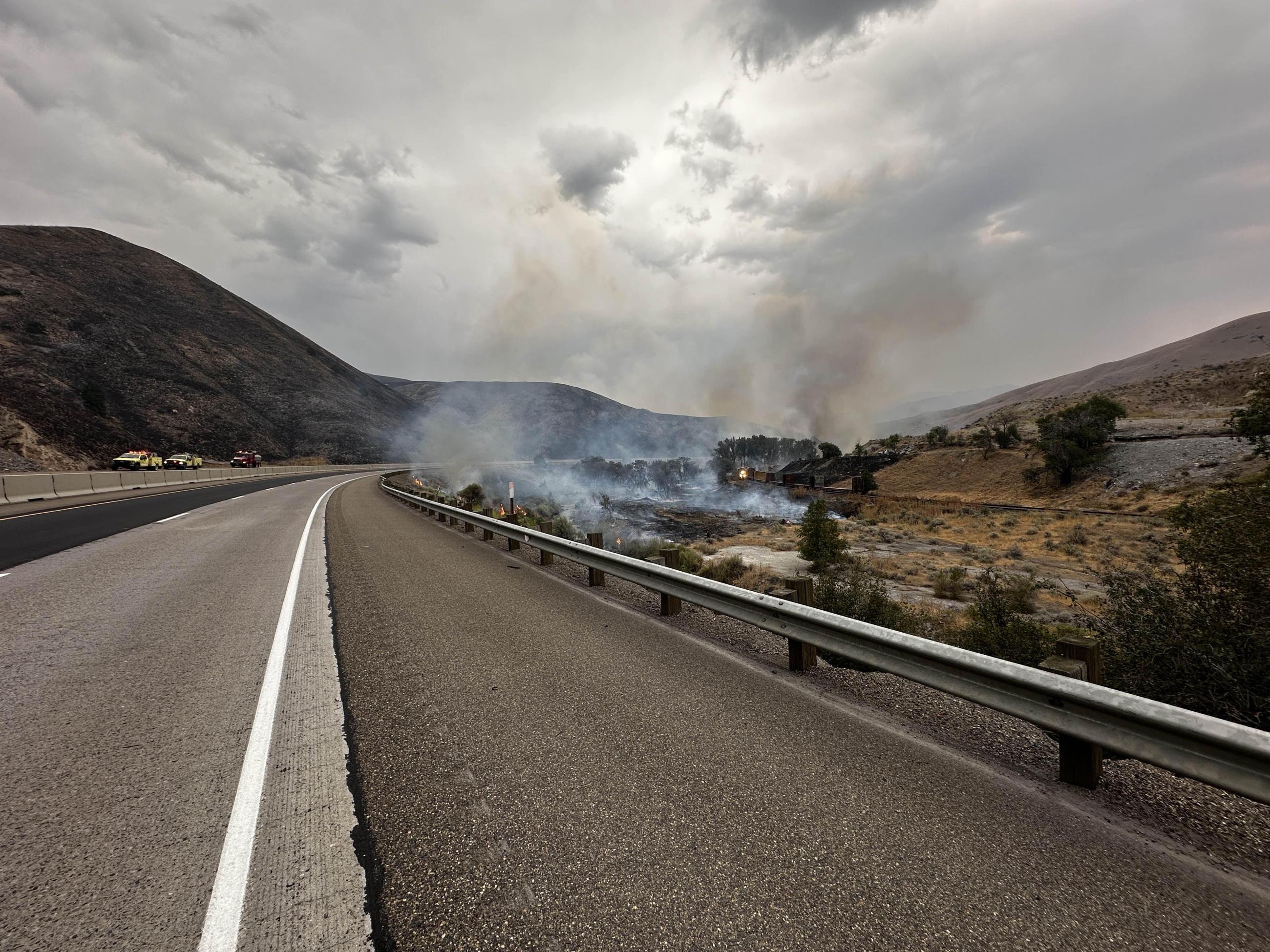 Smoke rises from active fire along interstate, fire engines seen in the background