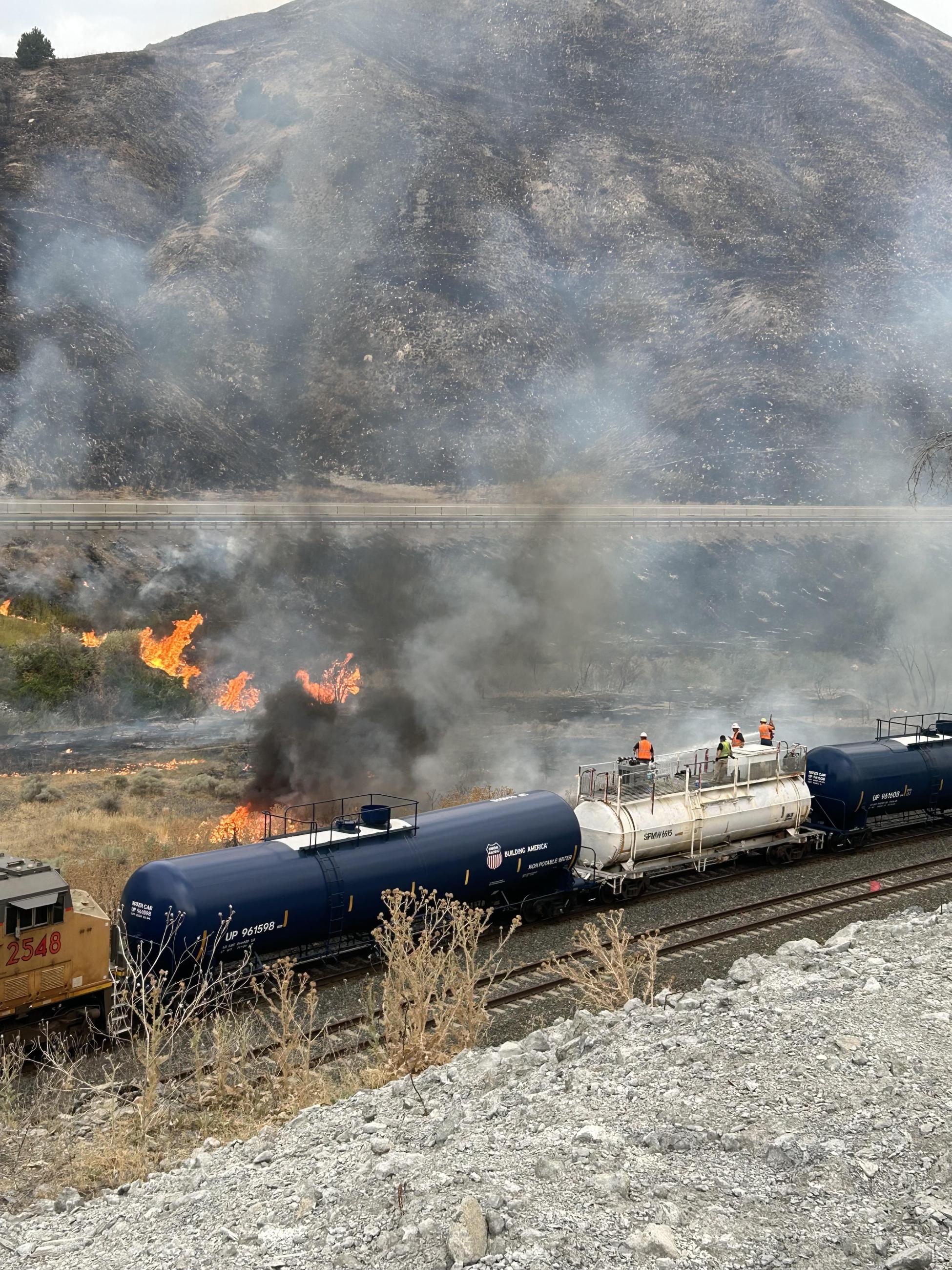Firefighters spraying water off a train, into flames