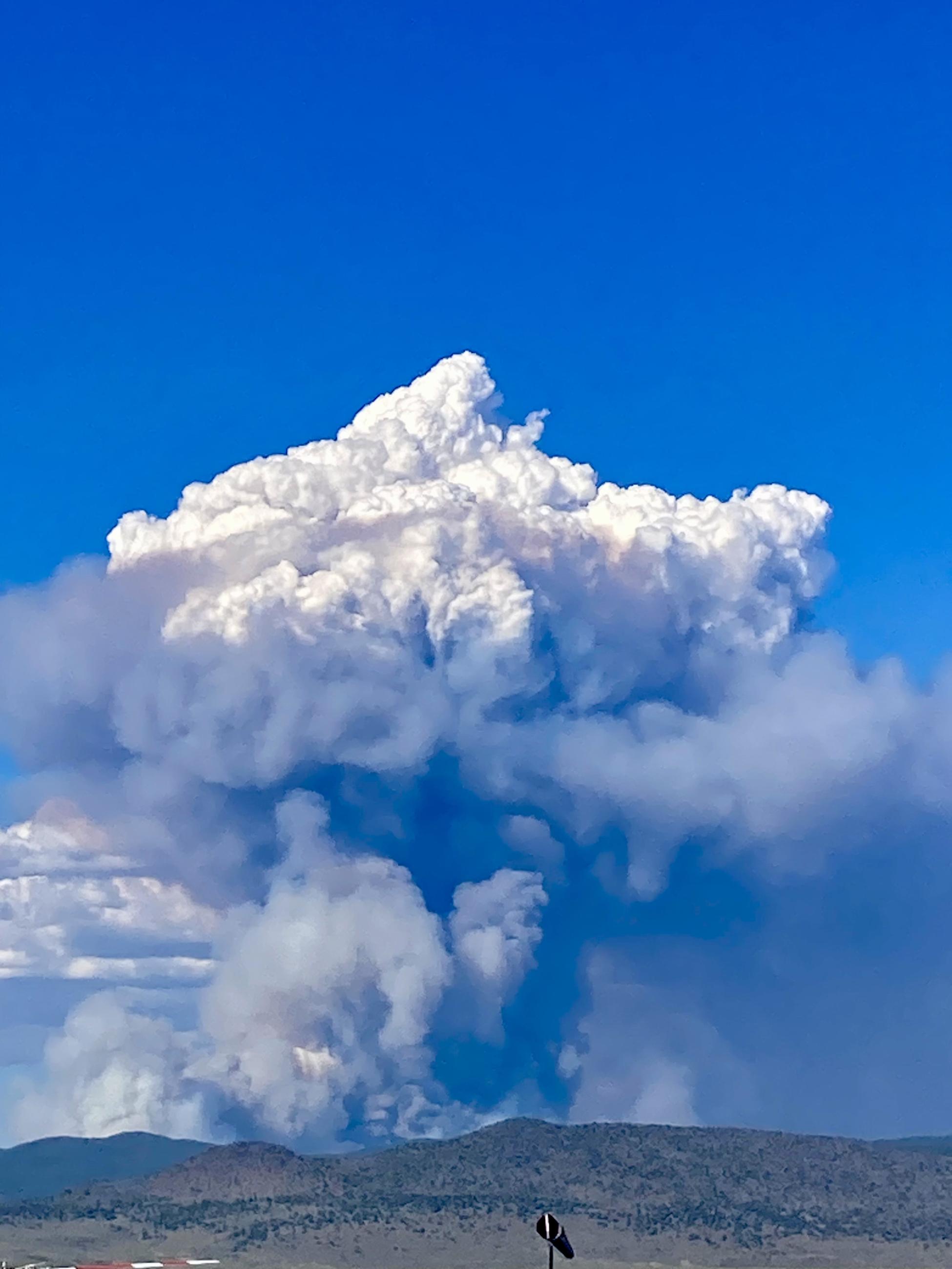 Mushroom cloud shaped smoke plume rising from distant hillside.