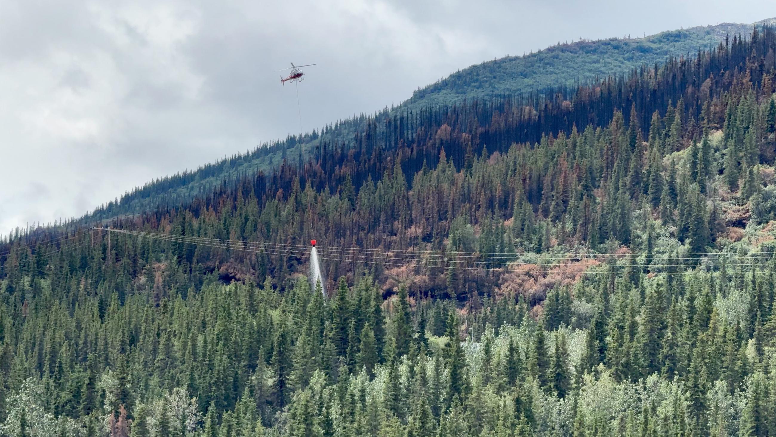 A helicopter making a water drop on the edge of the fire along the powerline corridor.