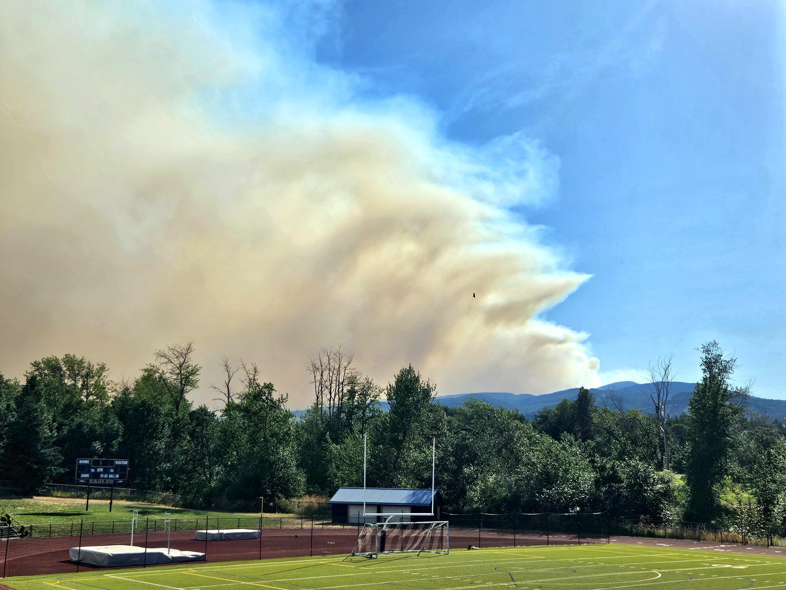 A brown smoke plume rises from the mountains in the distance.