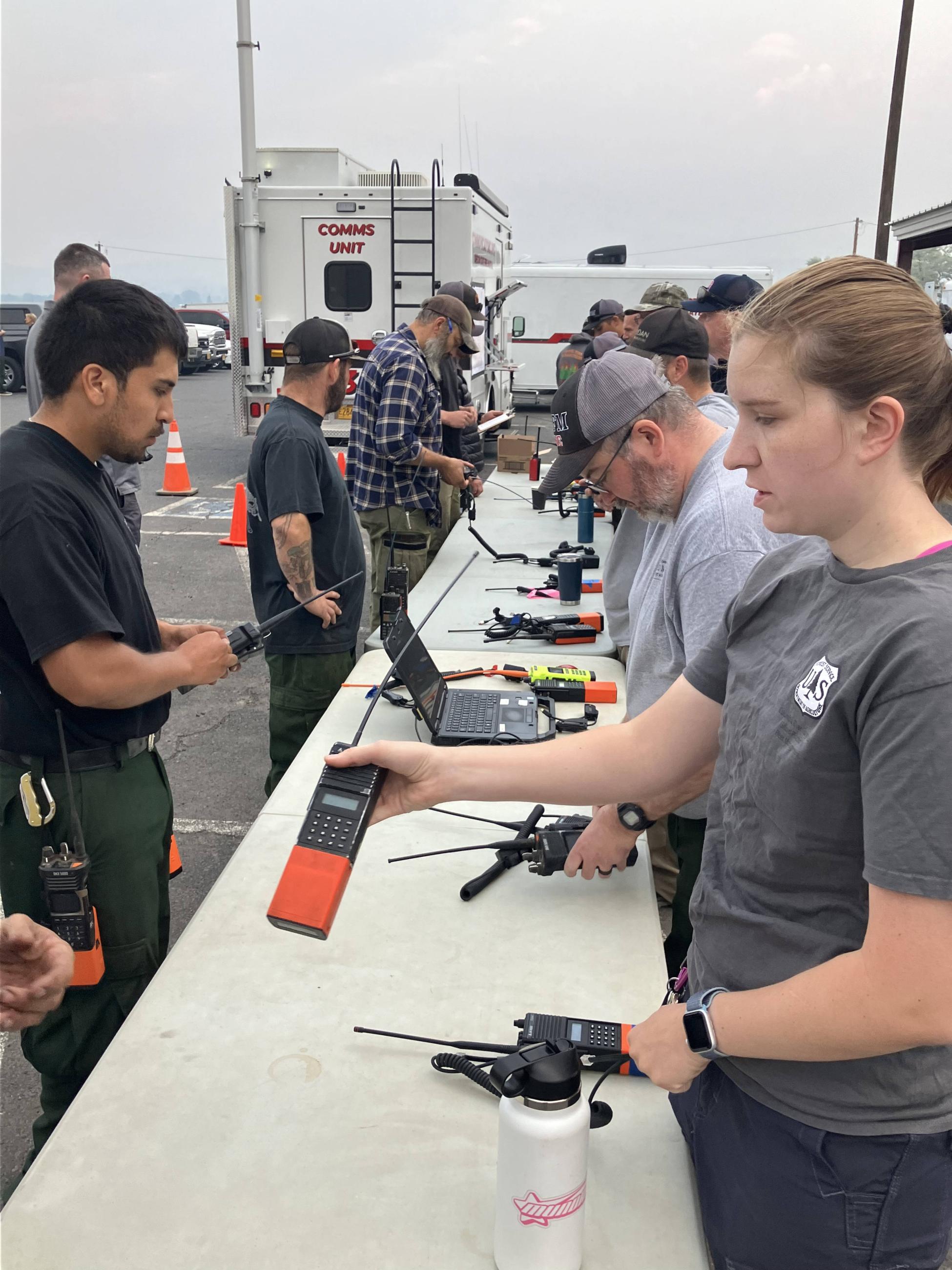 Firefighters and radio technicians conduct Radio Cloning at a long table at Falls Fire ICP