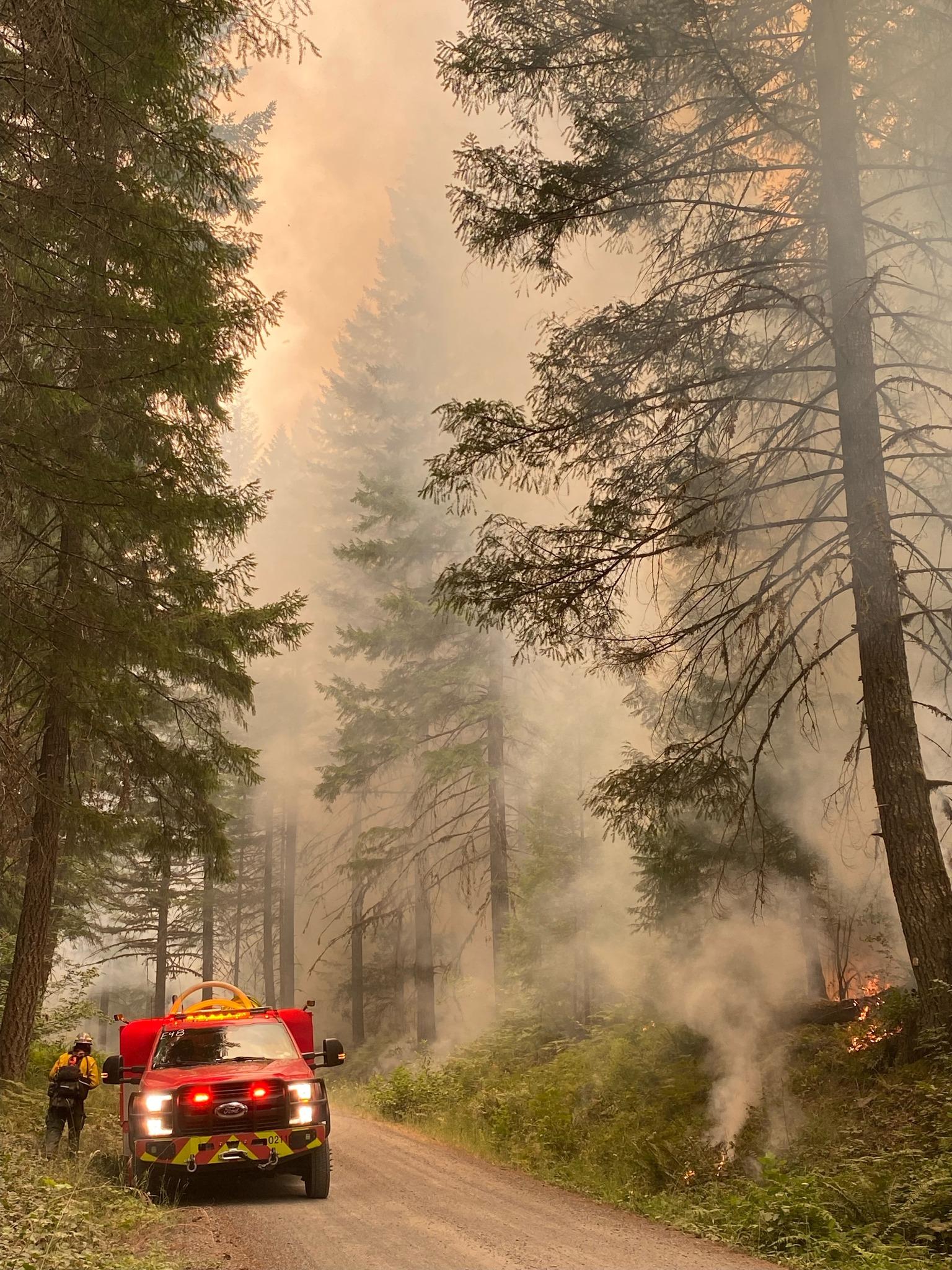 a firefighter and engine along a smoky road during a firing operation on the chalk fire