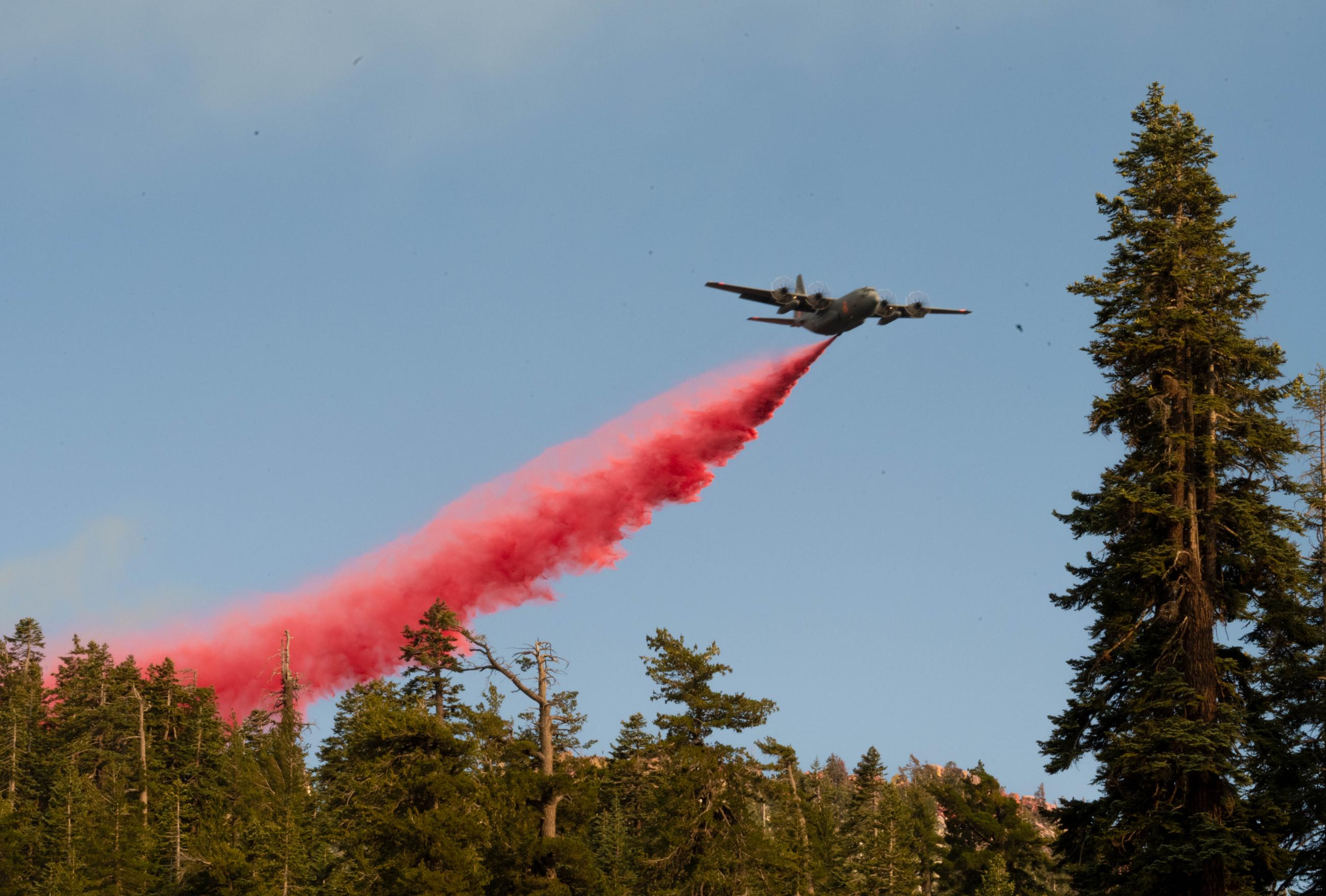 A plane flies over trees trailing a red cloud of retardant.