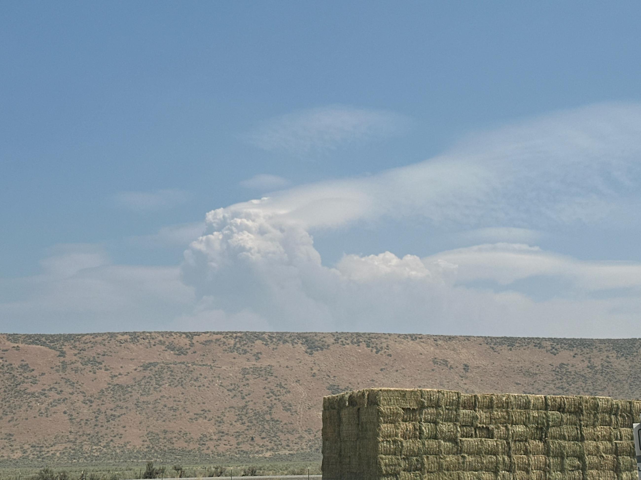 Fire smoke behind hills and stacked hay in the front