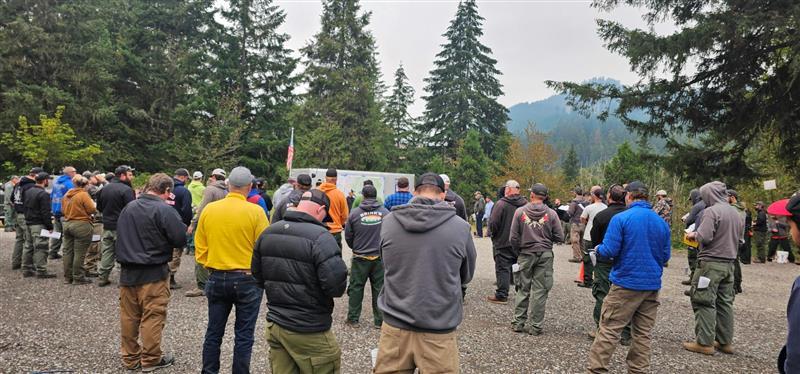 firefighters group together outside to listen to information provided at morning briefing