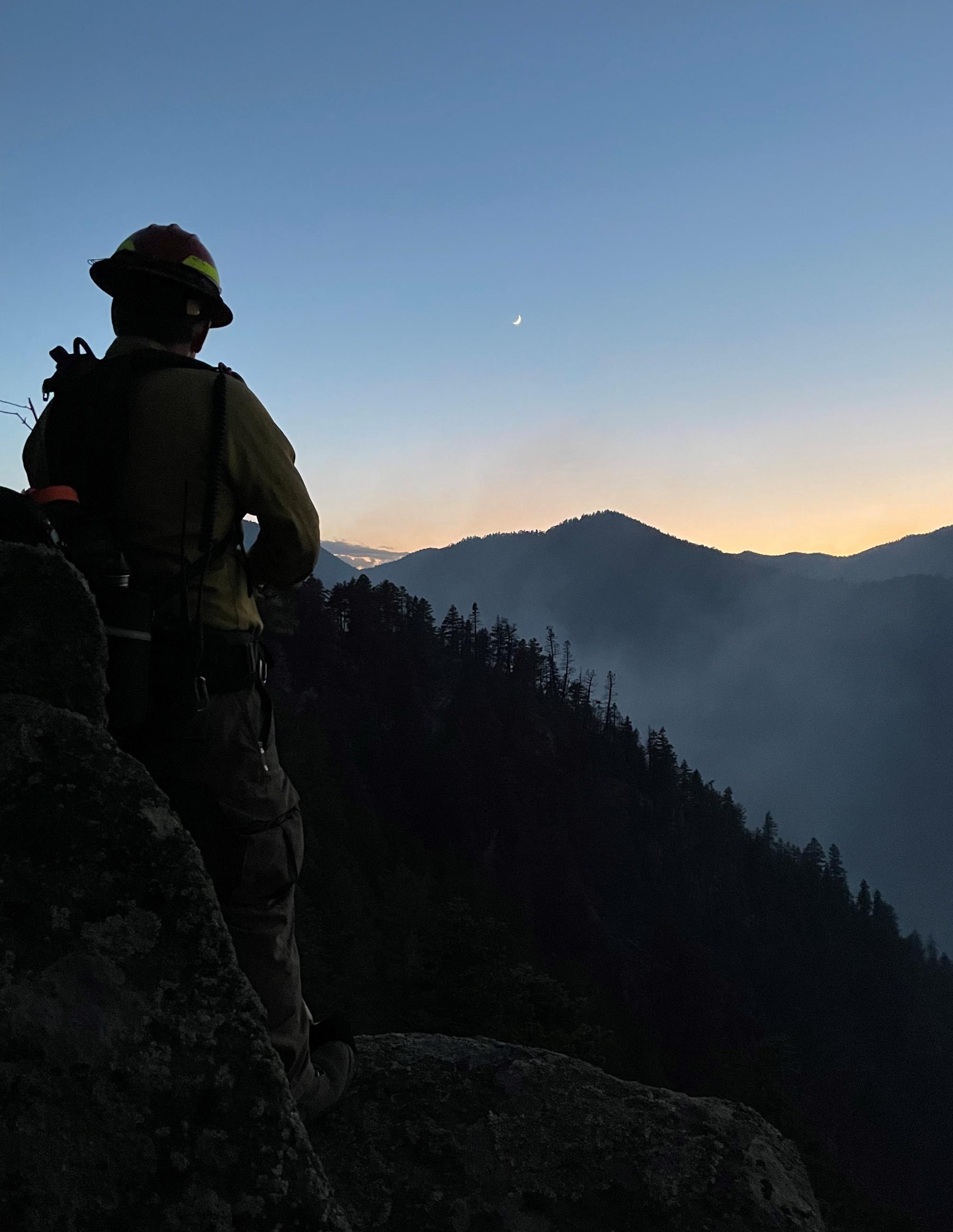 Image firefighter on a rock outcropping looking at the Oak Ridge Fire and sunset